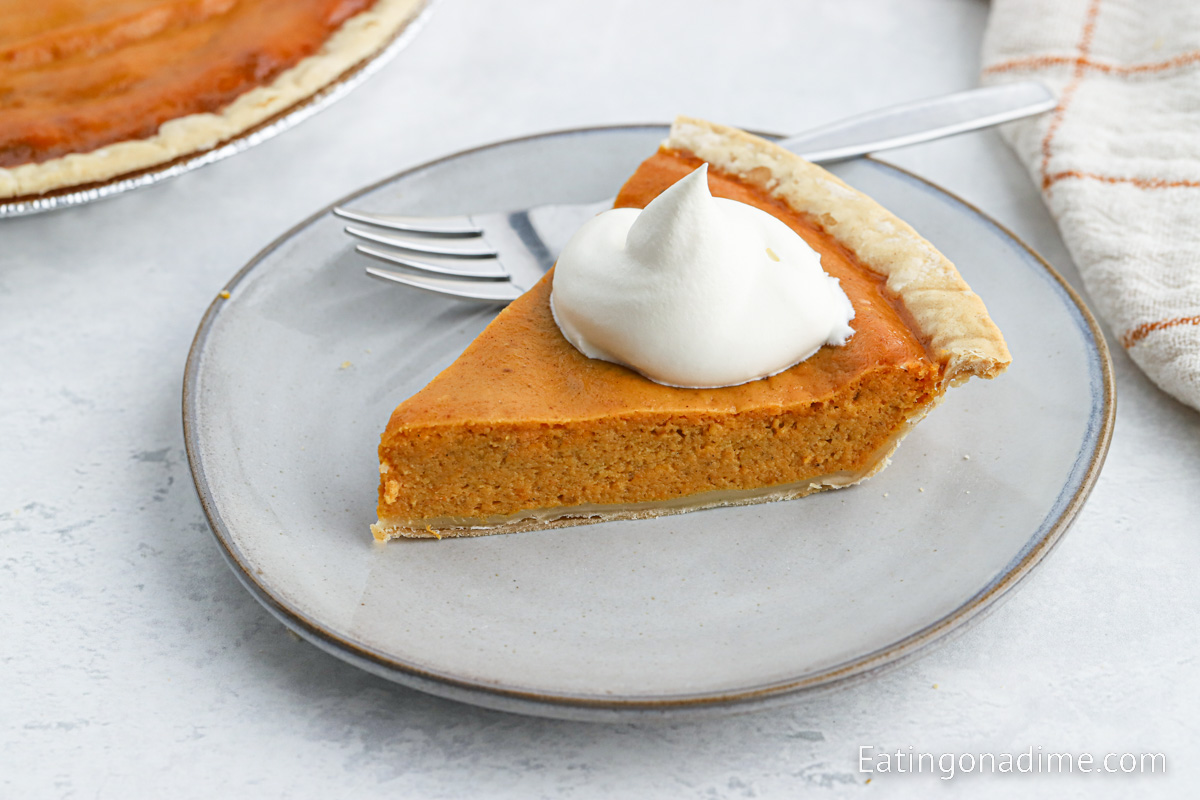 Slice of pumpkin pie on a plate topped with whipped cream