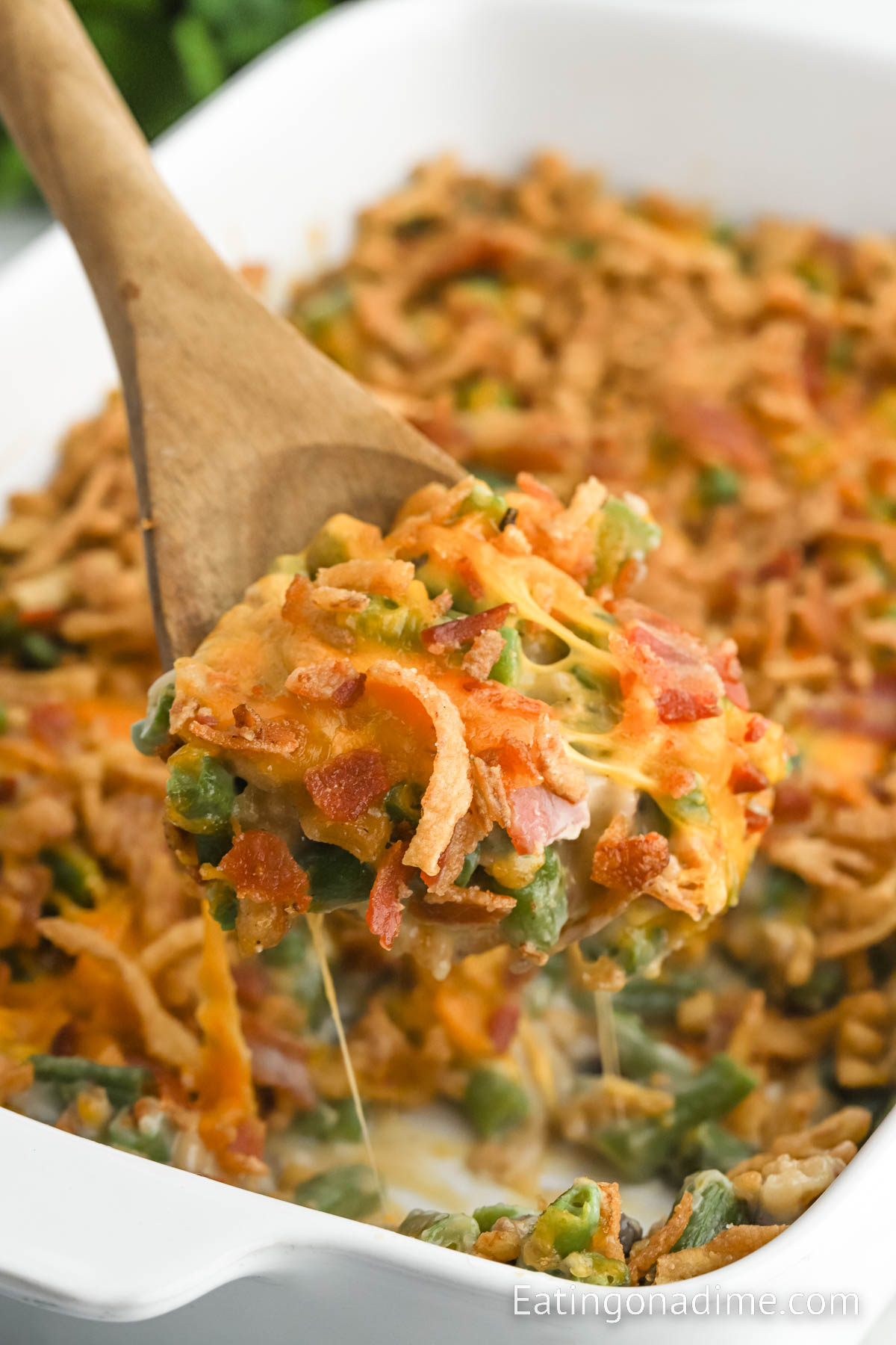 Close up image of green bean casserole with bacon and cheese with a wooden spoon