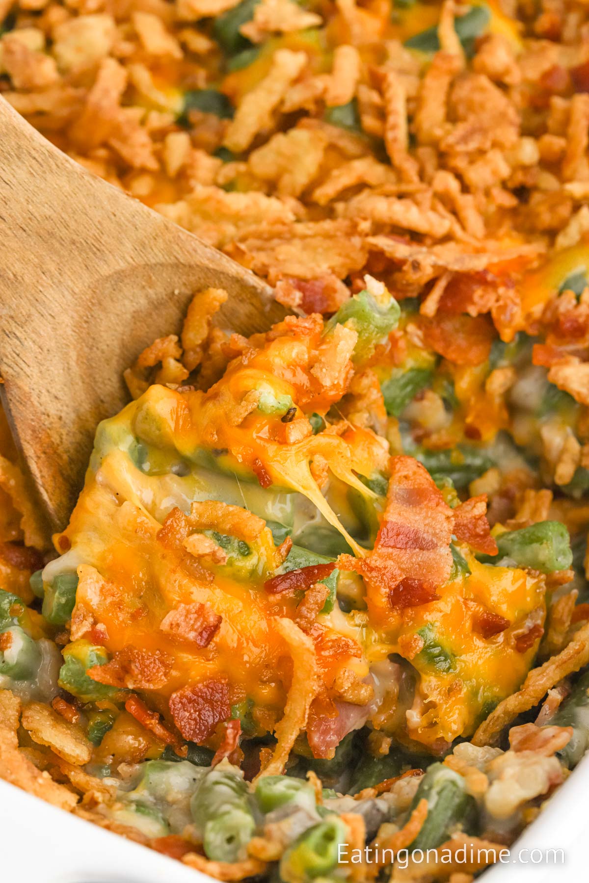 Close up image of green bean casserole with bacon and cheese with a wooden spoon