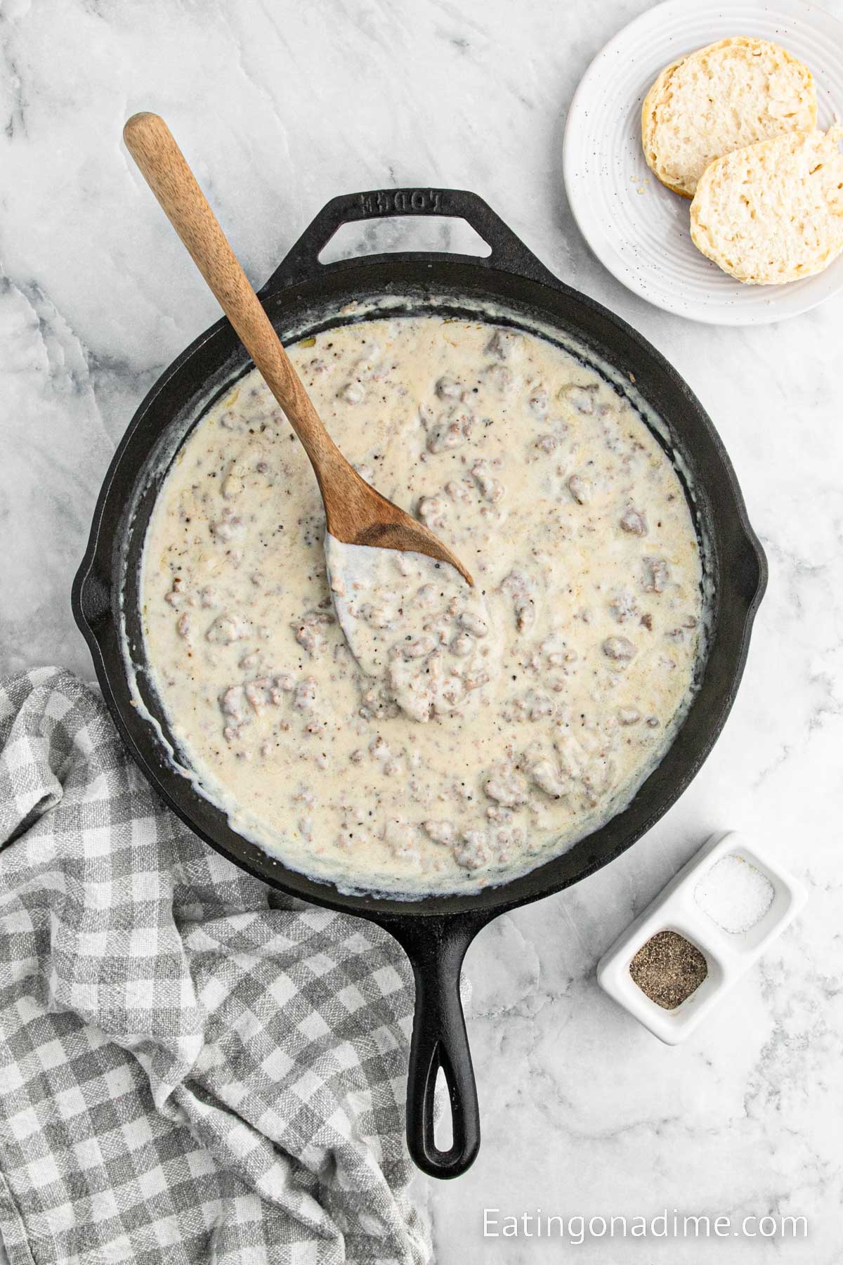 Sausage Gravy cooking in a cast iron skillet with a wooden spoon