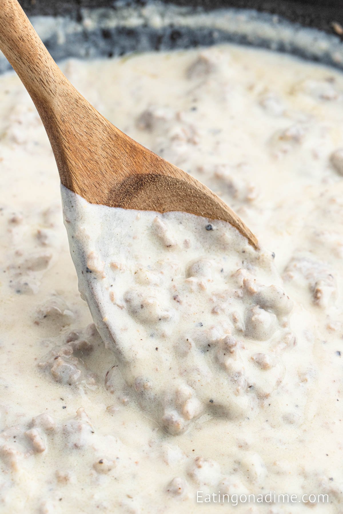 Sausage gravy in a skillet with a wooden spoon