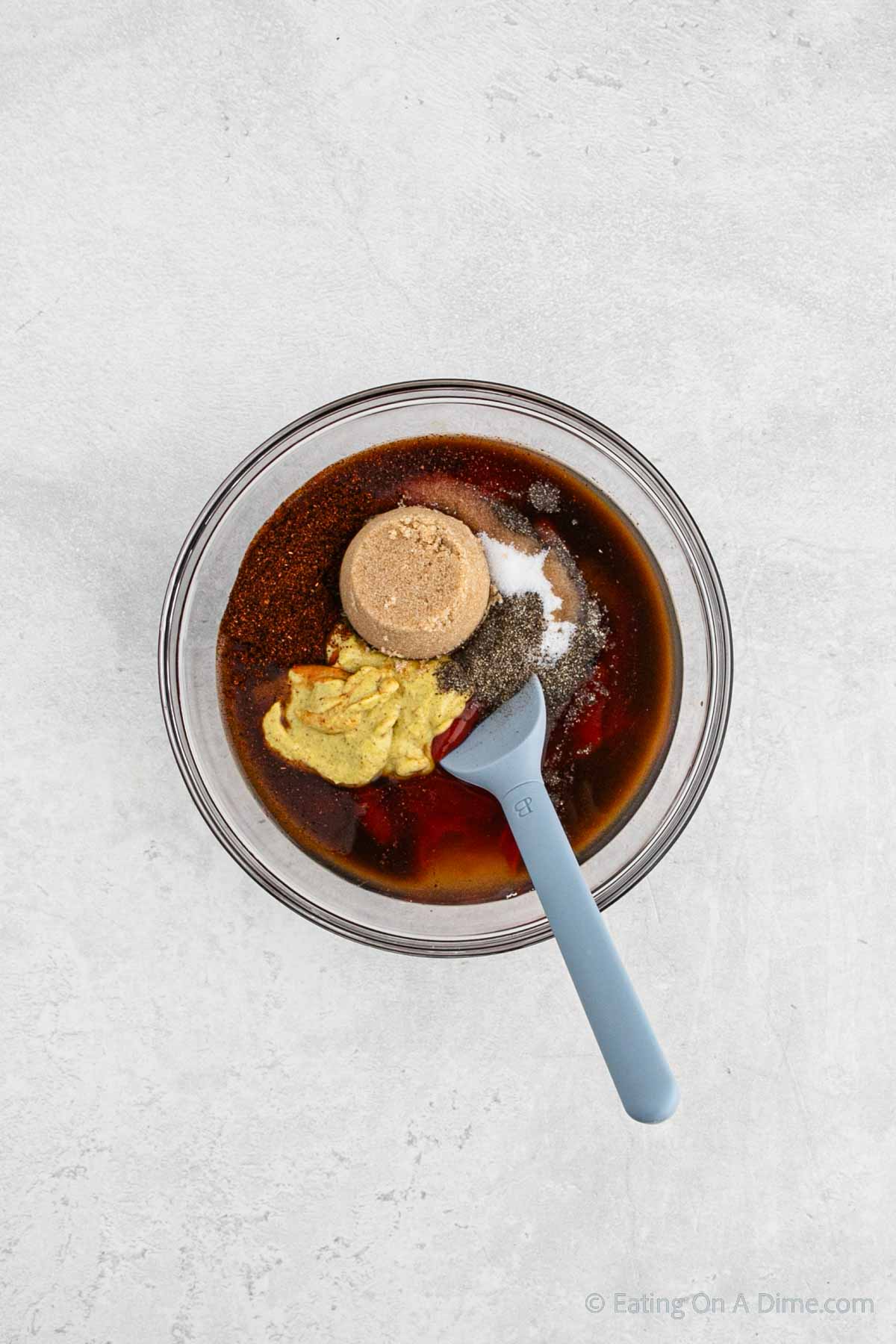 Combining the seasoning, brown sugar, mustard and ketchup with the apple cider vinegar in a bowl with a spatula