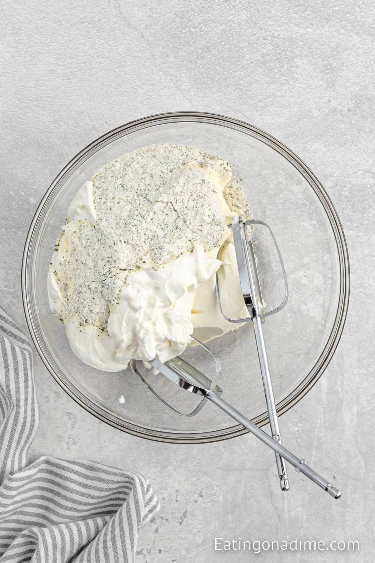 Beating cream cheese, sour cream, ranch dressing in a bowl