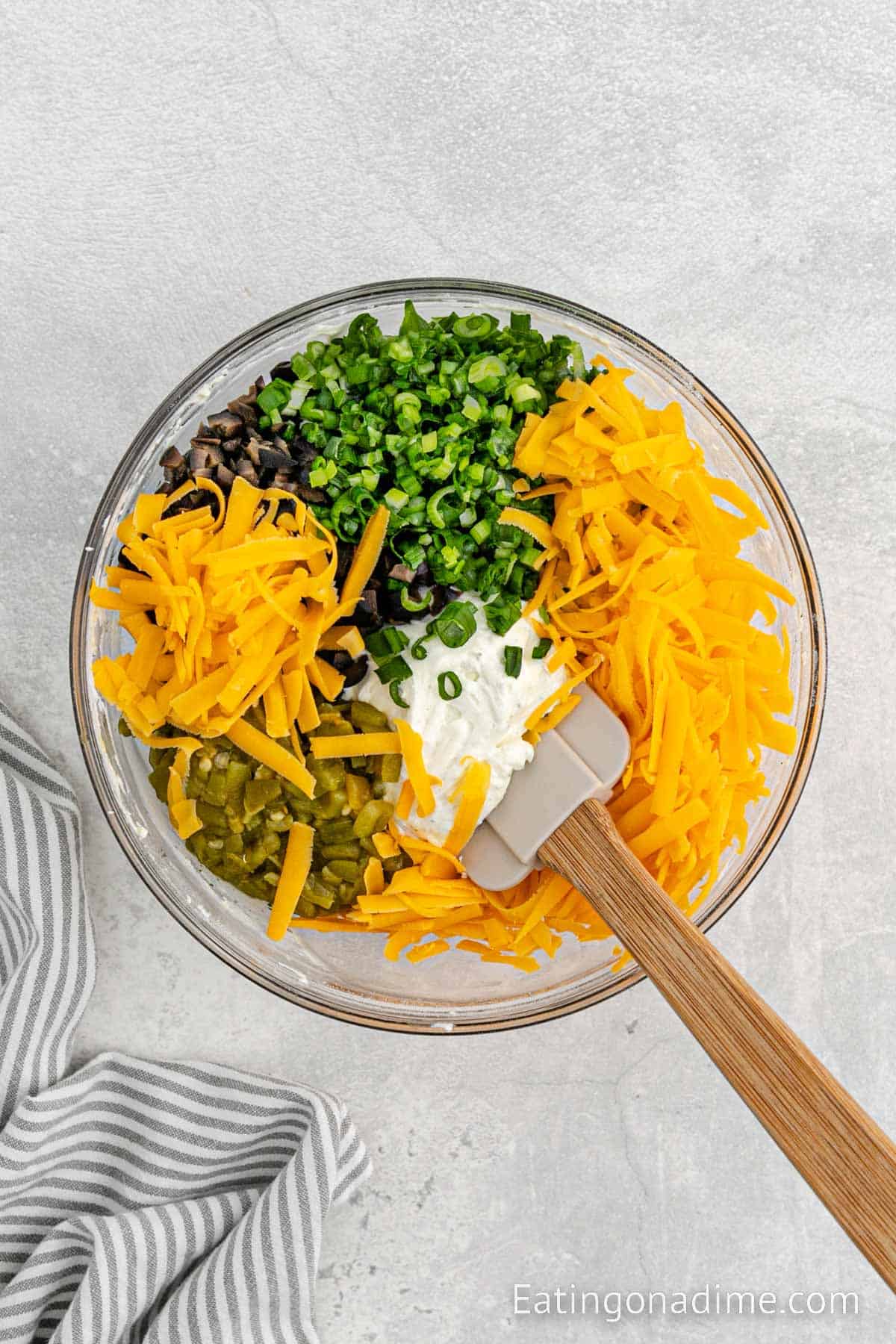 Adding shredded cheese, green chiles, green onions, and black olives to the cream cheese mixture