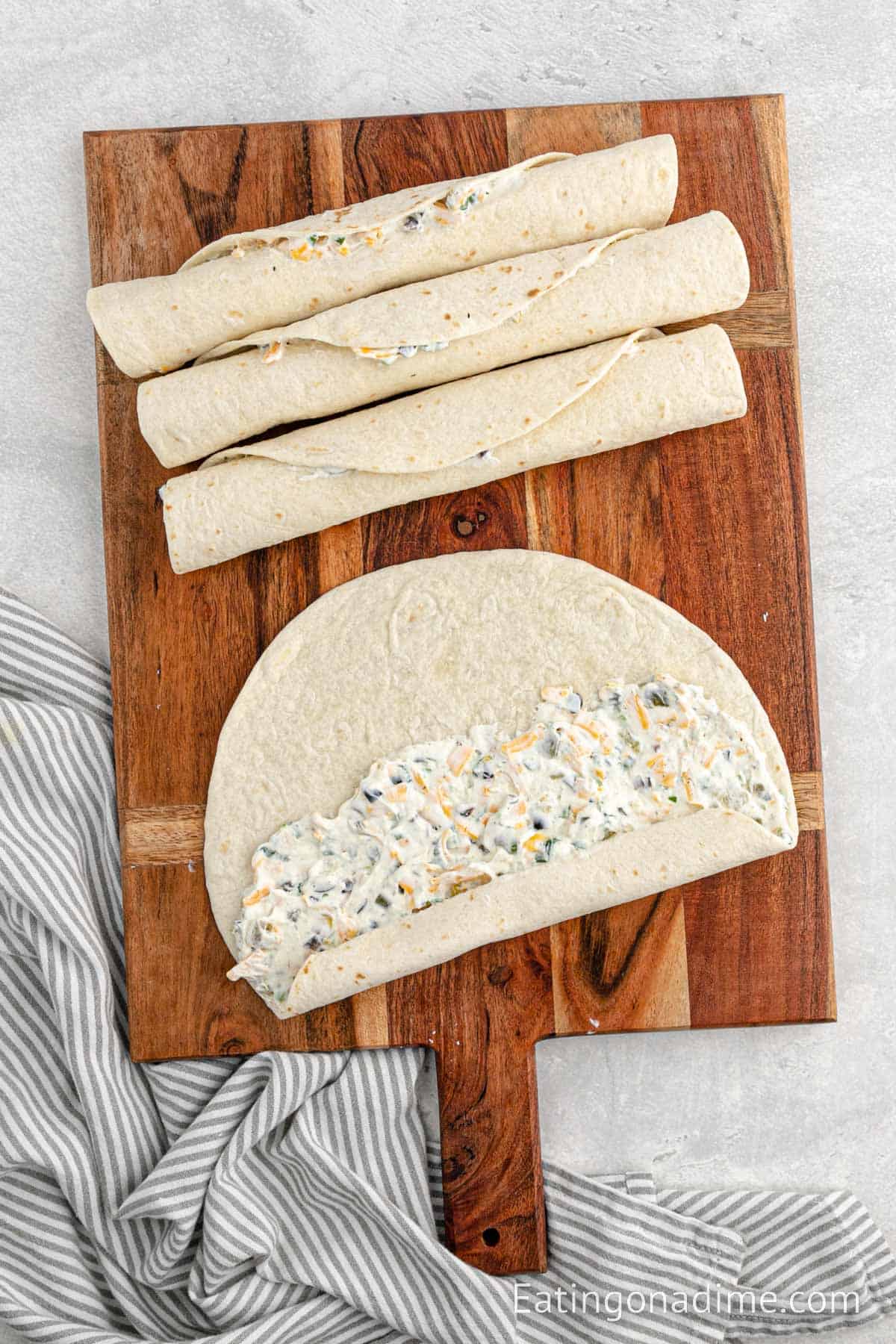 Spreading the cream cheese mixture on a tortilla and rolling the tortilla