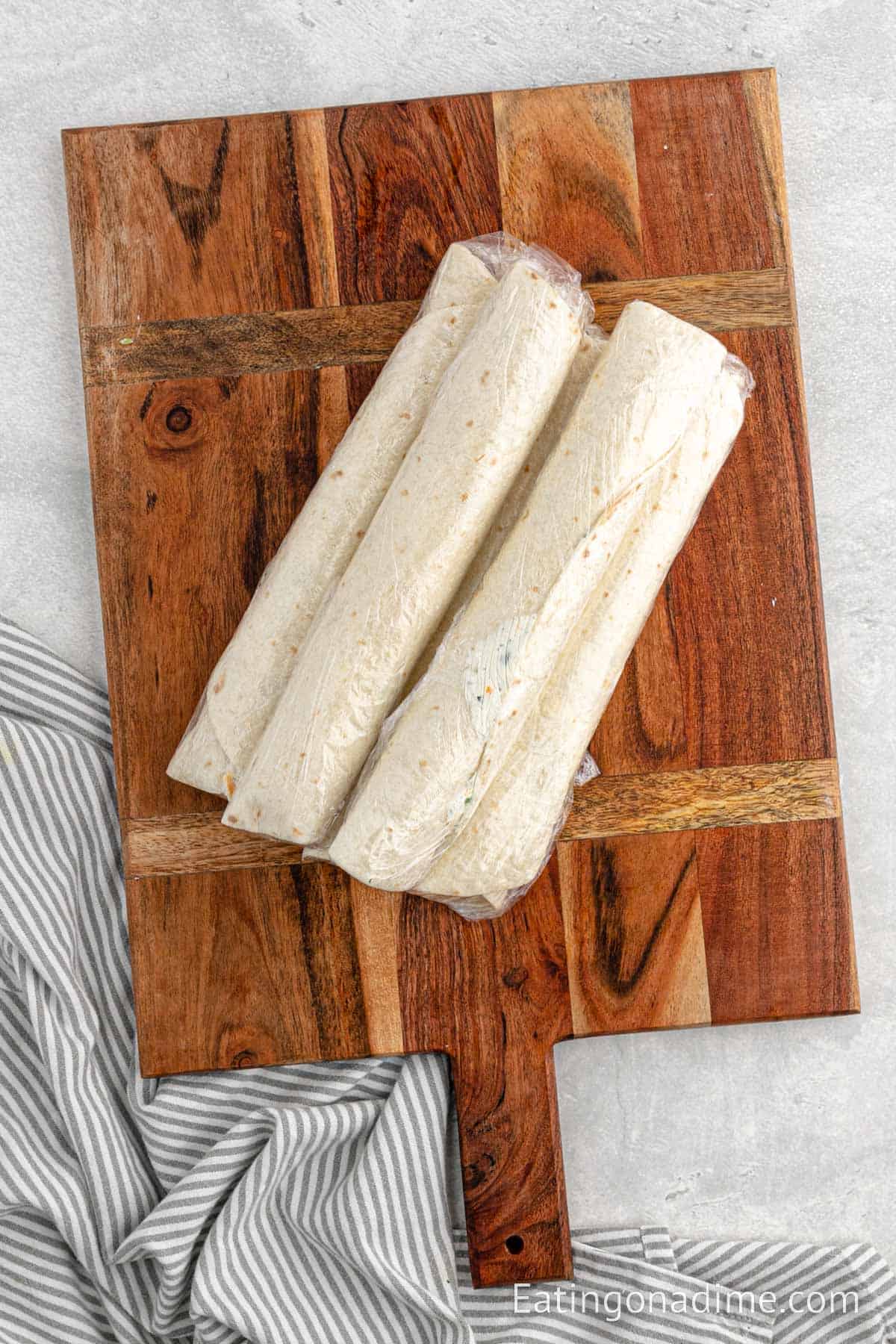 Wrapped tortilla in plastic wrap stacked on a cutting board