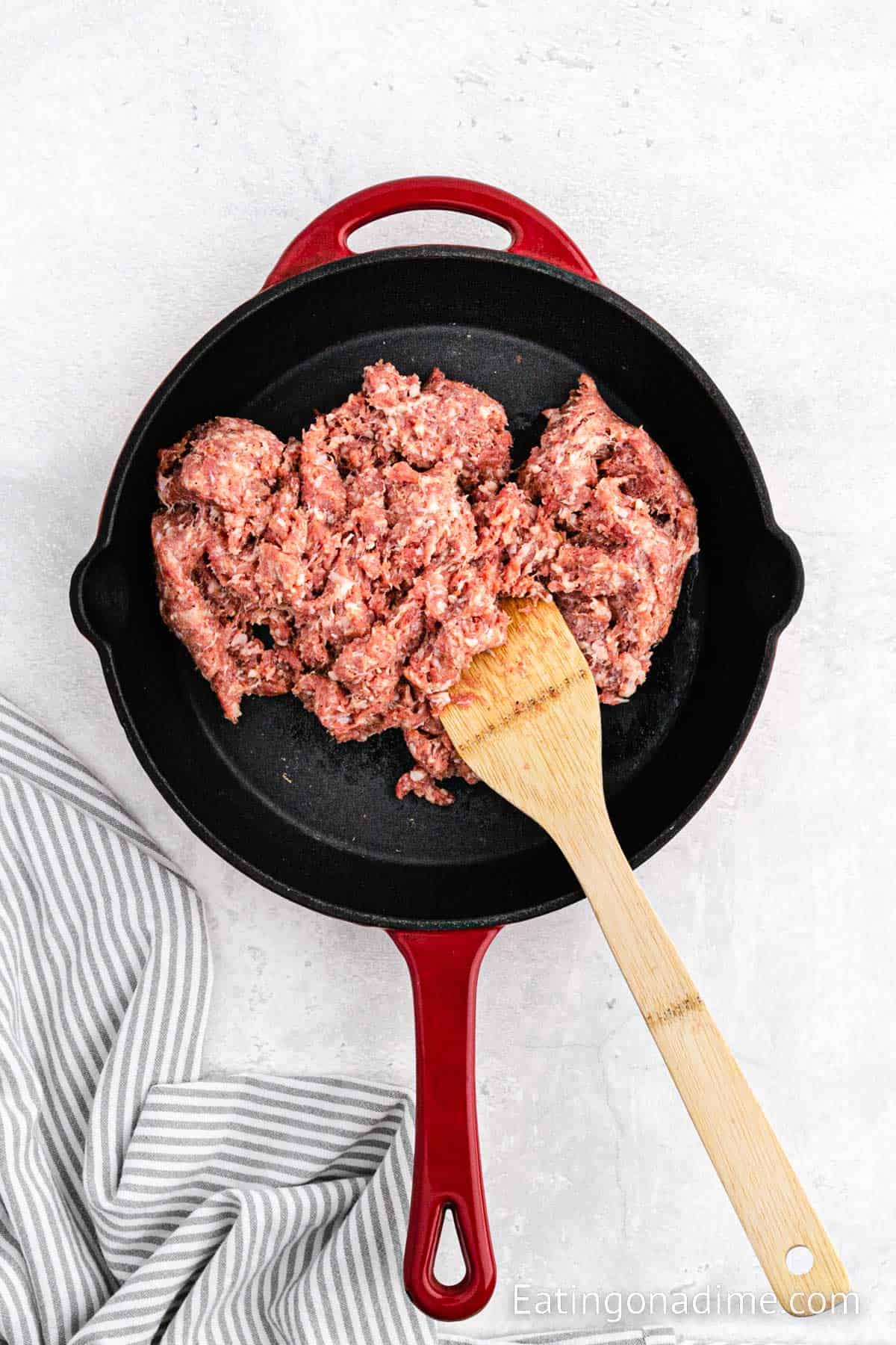 Cooking ground sausage in a cast iron skillet with a wooden spoon