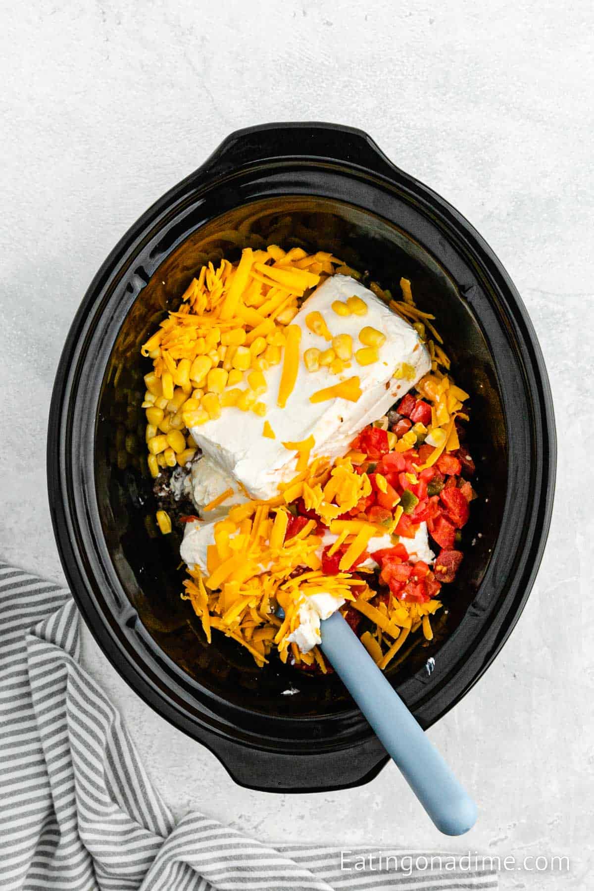Corn, cream cheese, Rotel and sausage in the slow cooker with a blue spatula