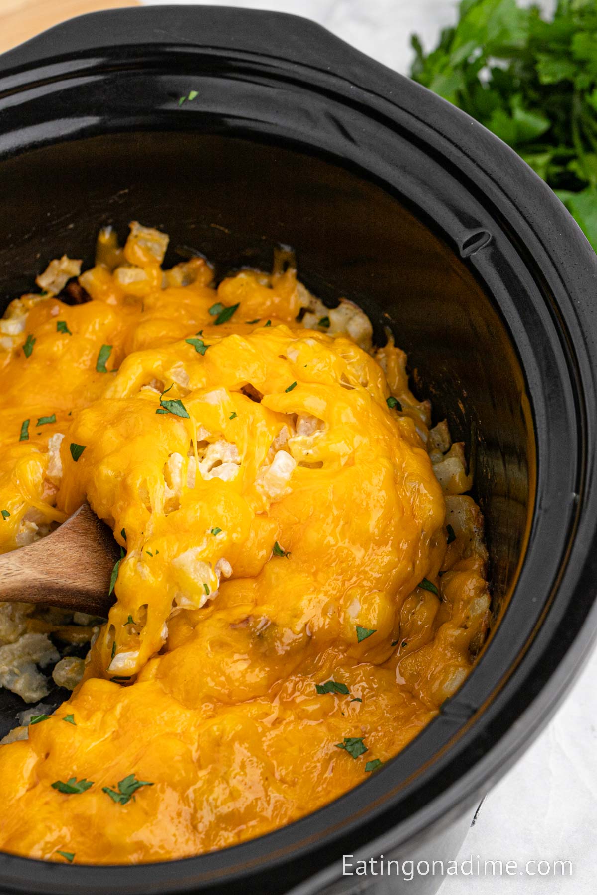 Funeral potatoes in a slow cooker with a wooden spoon