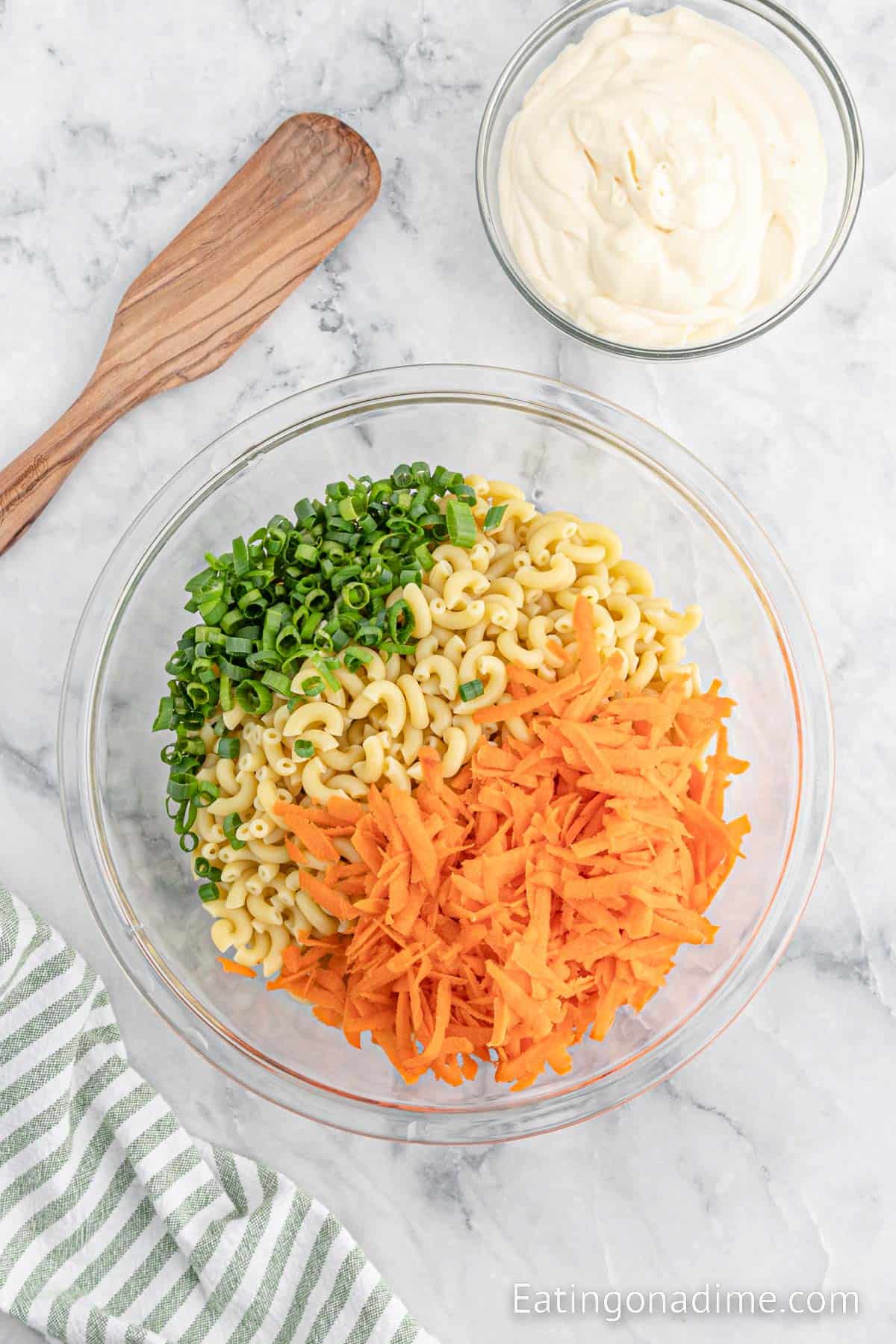 Chopped green onions, cooked macaroni noodles, and shredded carrots in a bowl with a bowl of mayonnaise on the side