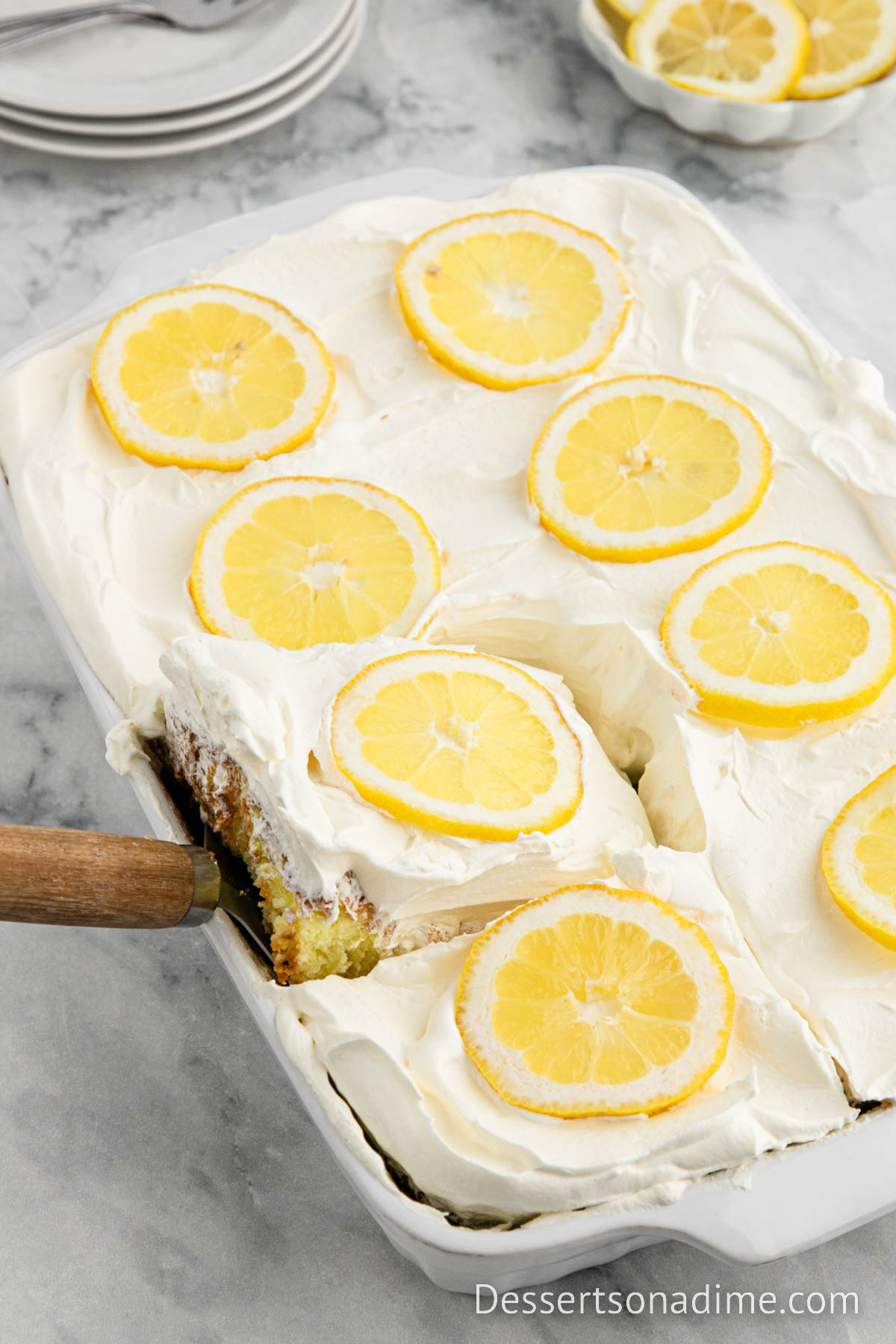 Lemon Angel Food Cake in a baking dish topped with cool whip and slice lemons