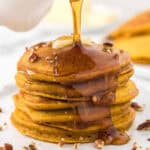 Close up image of stacked pumpkin pancakes with syrup and chopped pecans.