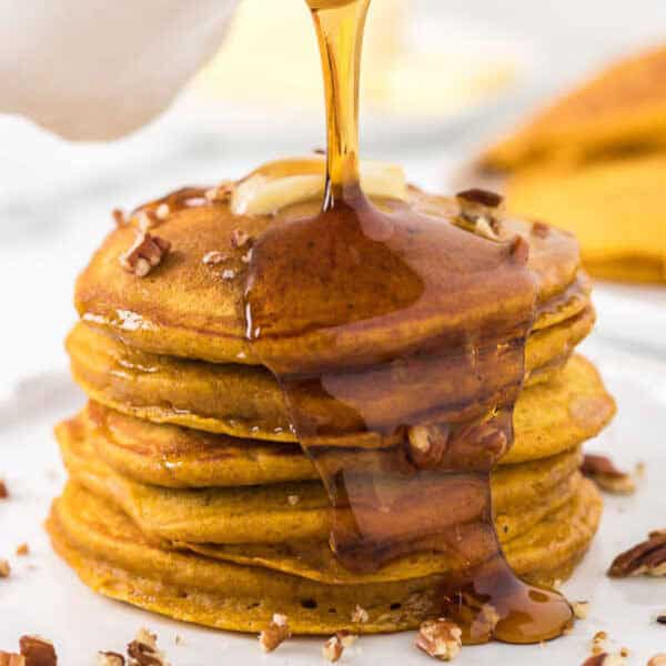 Close up image of stacked pumpkin pancakes with syrup and chopped pecans.