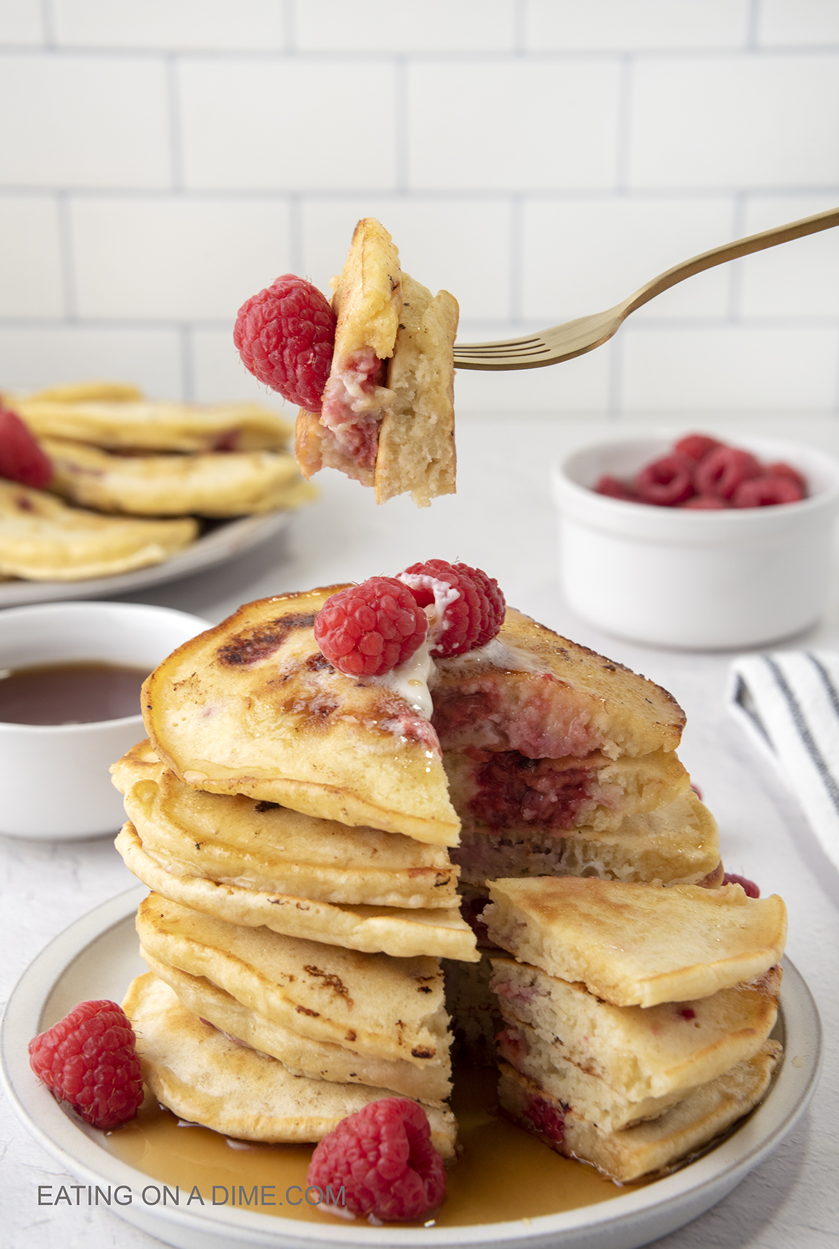 Raspberry pancakes stacked on a plate with a bite on a fork