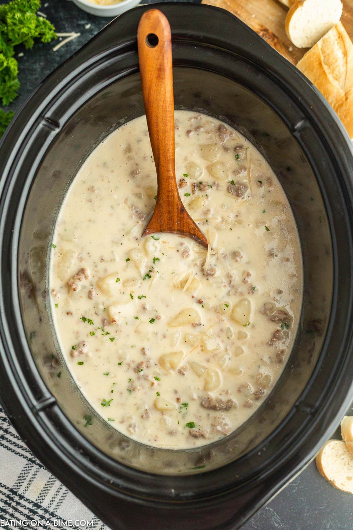 Crock pot with sausage potato soup with a wooden spoon