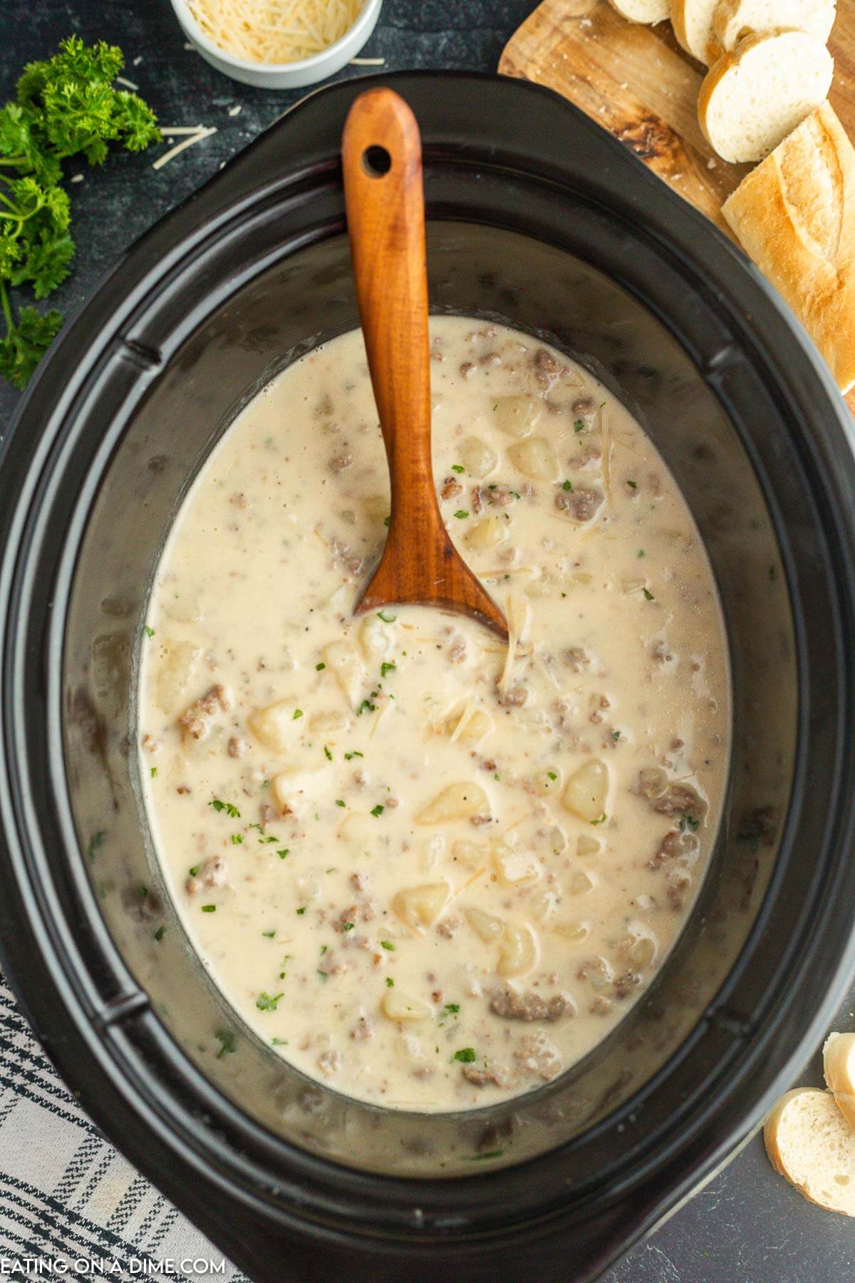 Crock pot with sausage potato soup with a wooden spoon