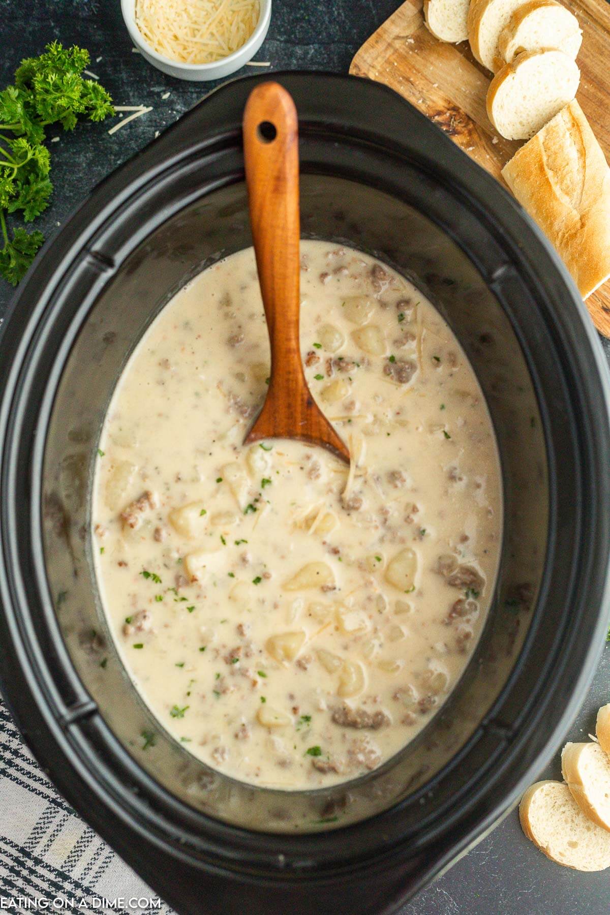 Crock pot with sausage potato soup with a wooden spoon