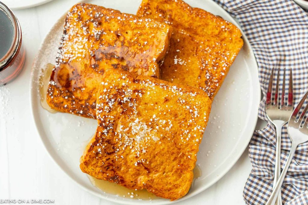French Toast stacked on a plate with powdered sugar and syrup