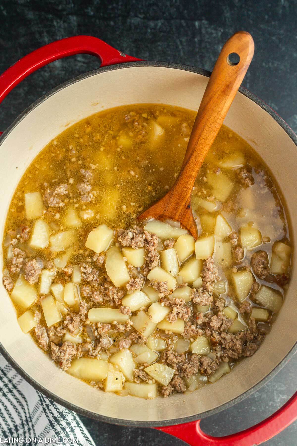 Sausage potato soup in a Dutch Oven with a wooden spoon