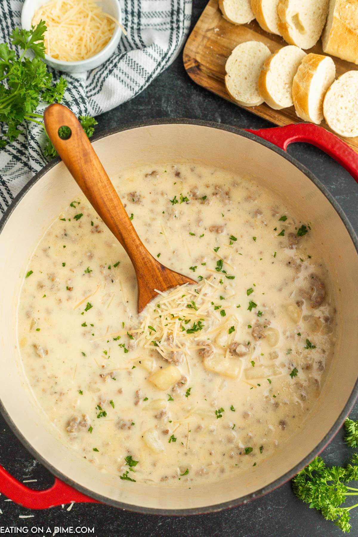 Sausage potato soup in a Dutch Oven with a wooden spoon