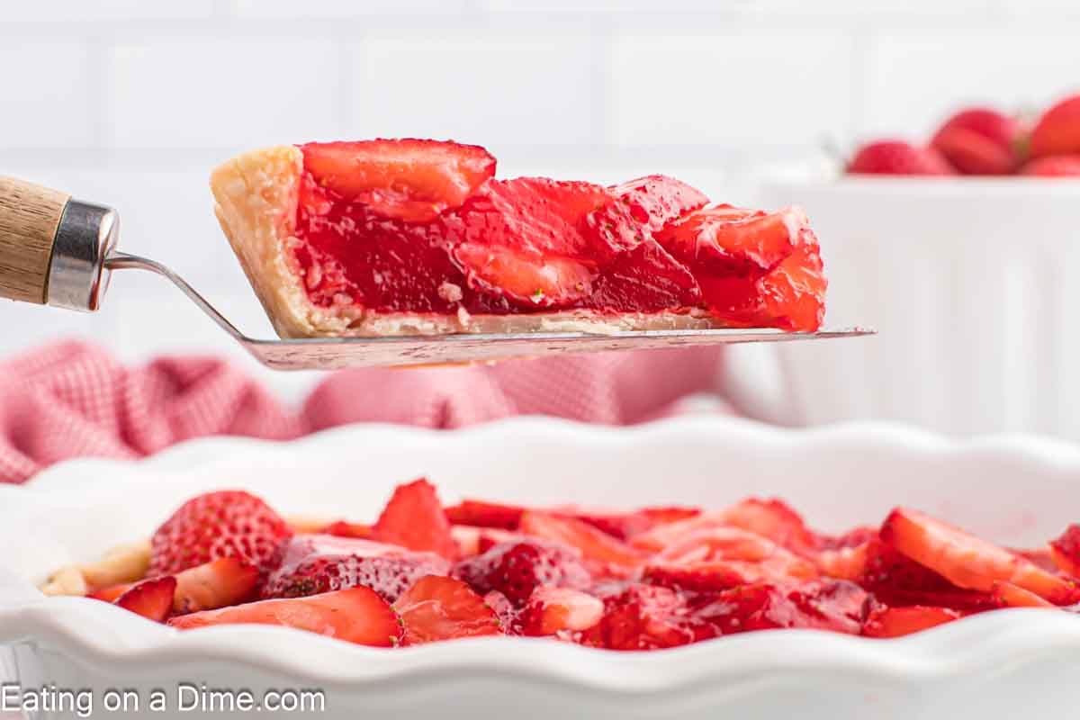 A slice of Strawberry Pie on a spatula over a whole strawberry pie.