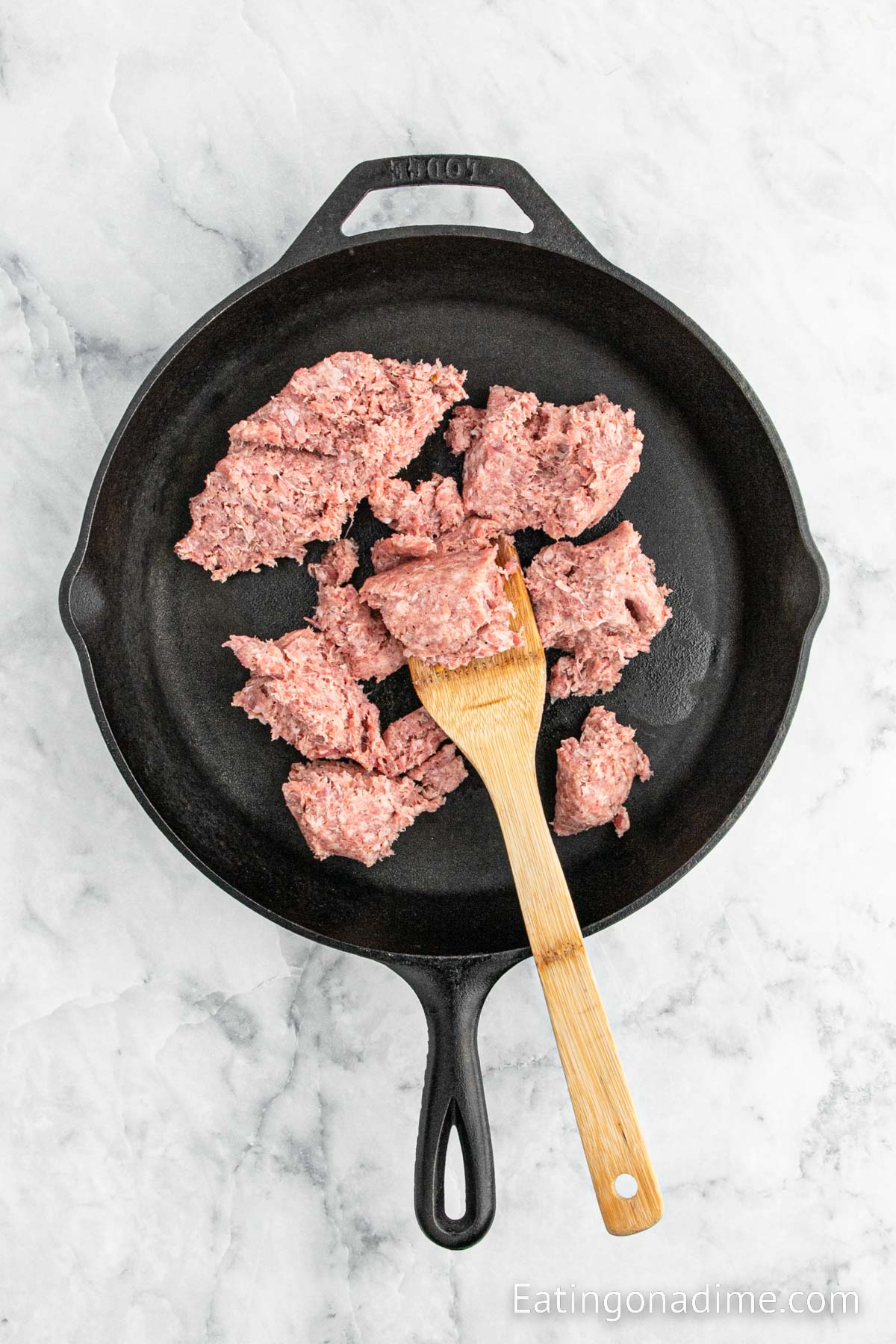 Cooking sausage in a cast iron skillet with a wooden spoon