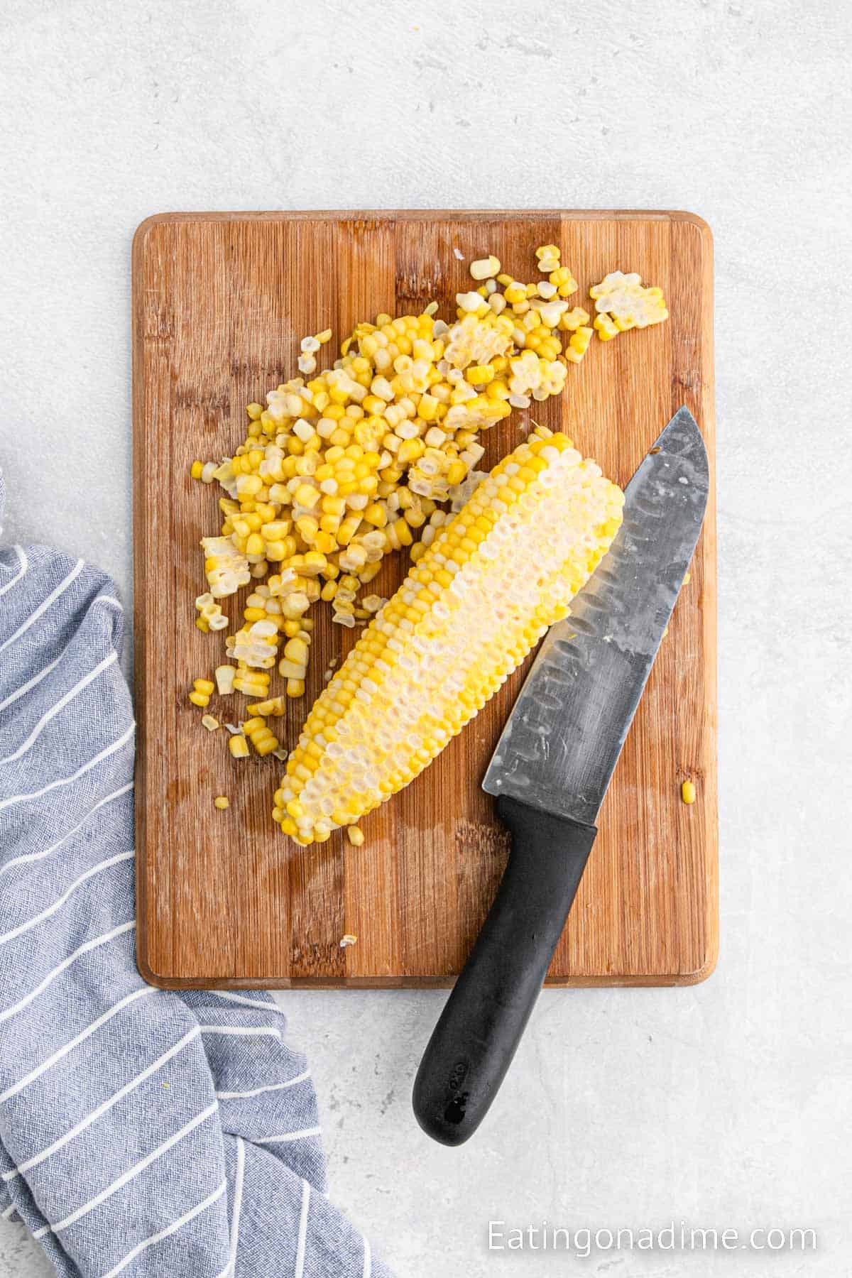 Cutting the corn kernels off the fresh corn on a cutting board and knife