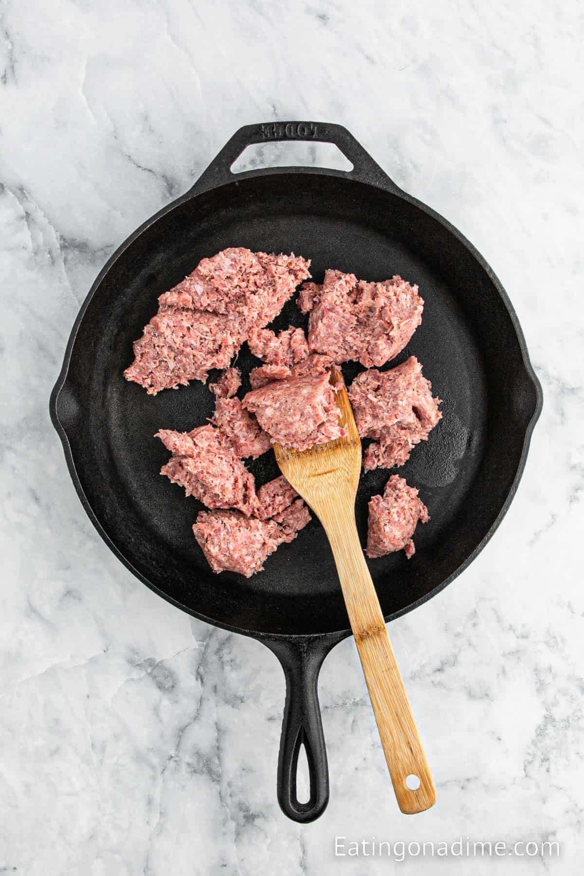 Ground Sausage in a cast iron skillet with a wooden spoon