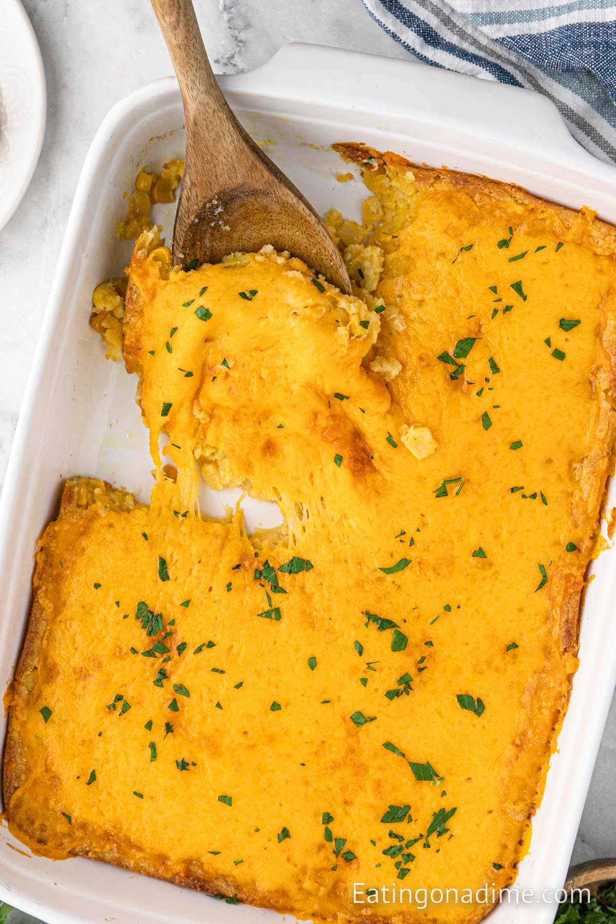Corn casserole in a casserole dish with a wooden spoon