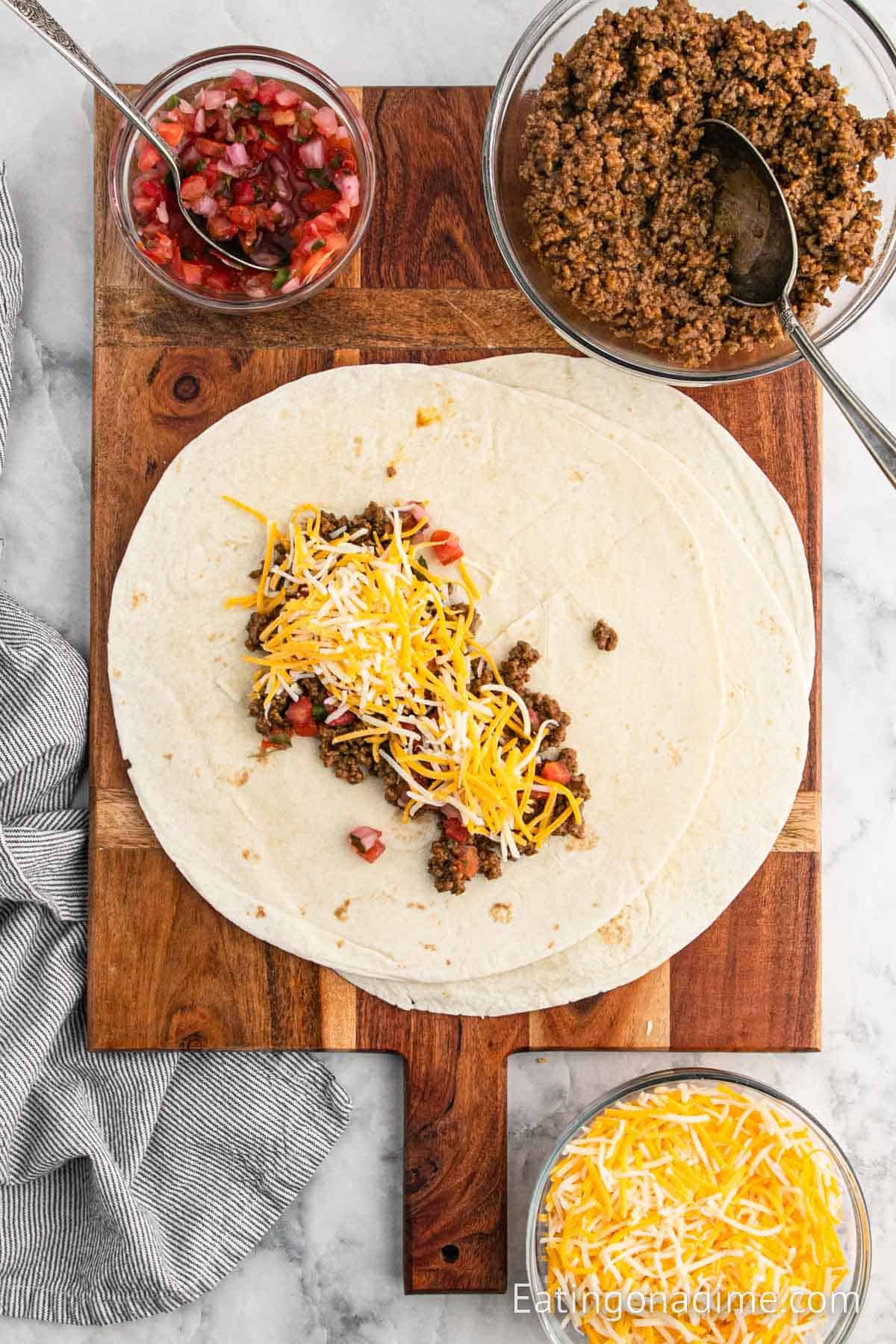 Topping a flour tortilla with ground beef, pico de gallo and cheese