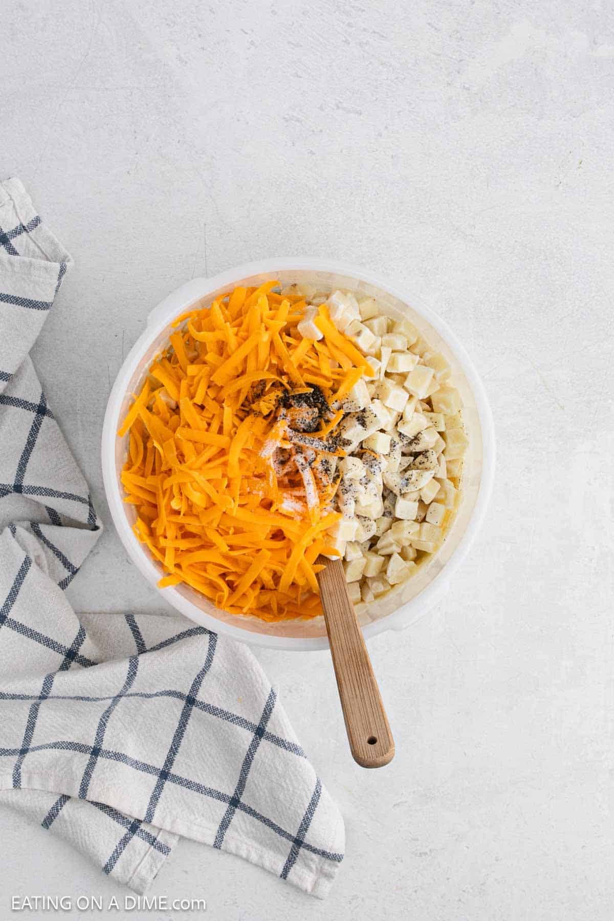 Shredded cheese, spices and hash browns added to a bowl.