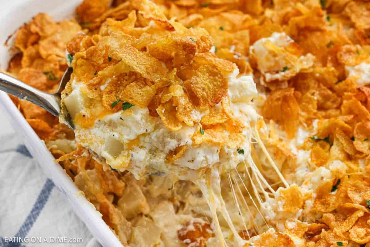 Funeral potatoes in a baking dish with a serving on a spoon ready to serve.