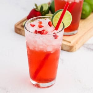 Strawberry drink in a clear glass with ice and topped with diced strawberries with a lime wedge on the rim of the glass.