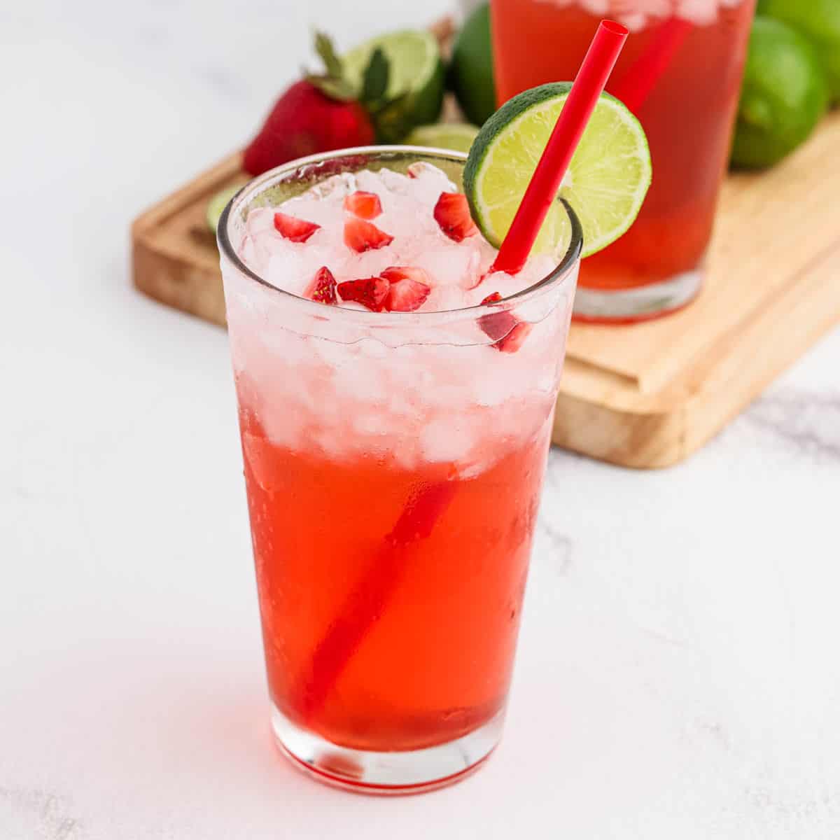 Strawberry drink in a clear glass with ice and topped with diced strawberries with a lime wedge on the rim of the glass.