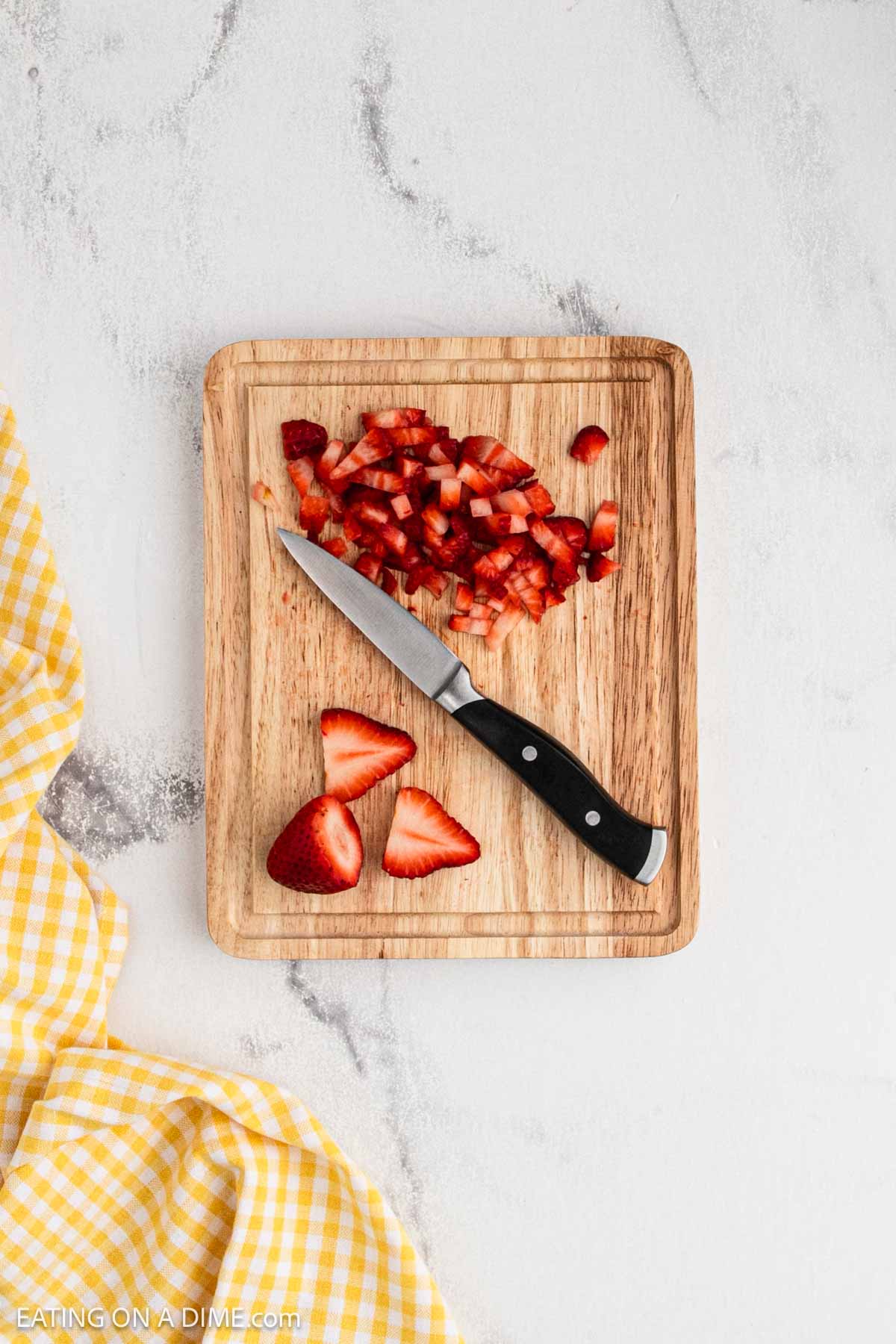 Fresh strawberries cut into small pieces on a cutting board with a knife.