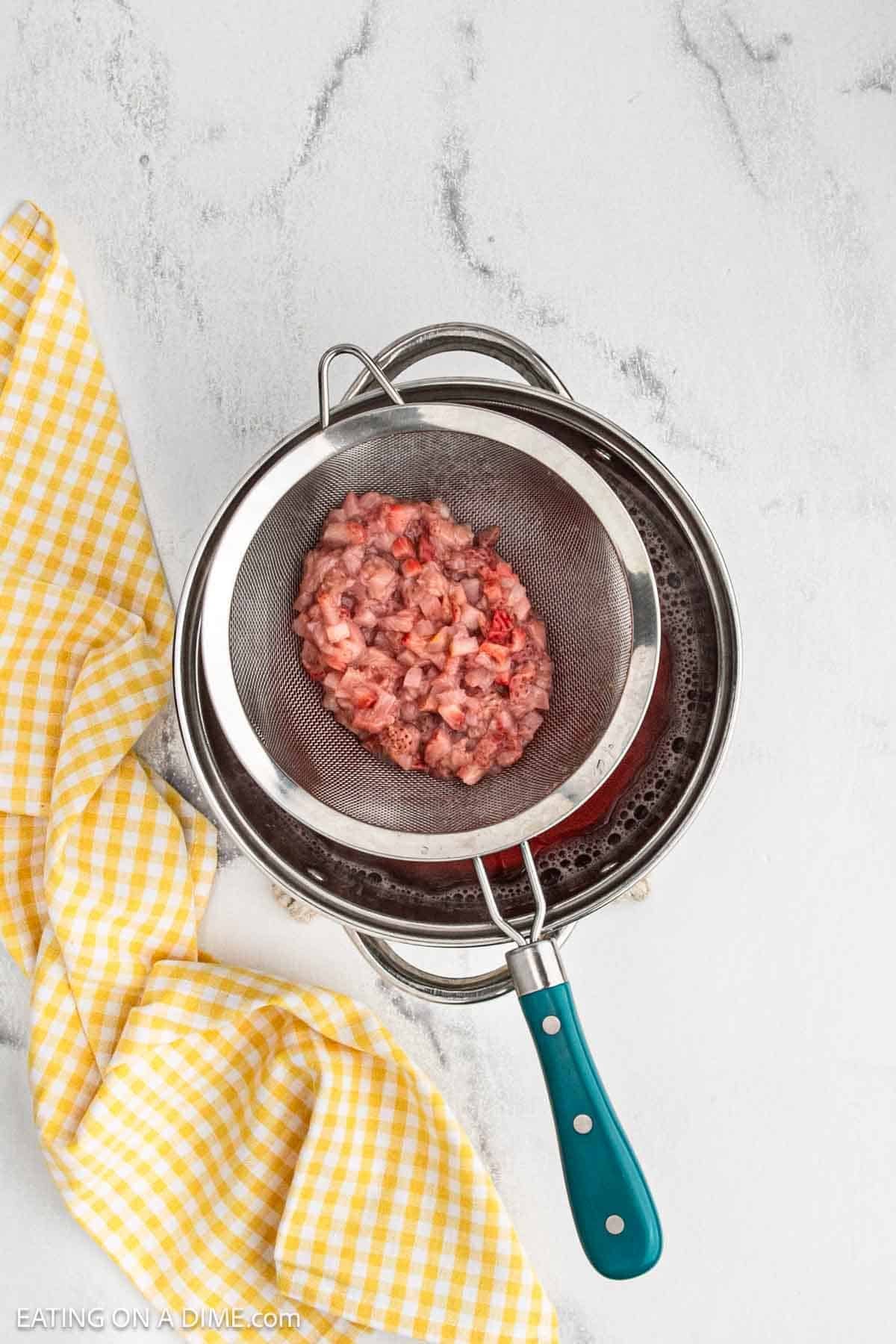 Cooked strawberries in a strainer over a large pot of liquid.
