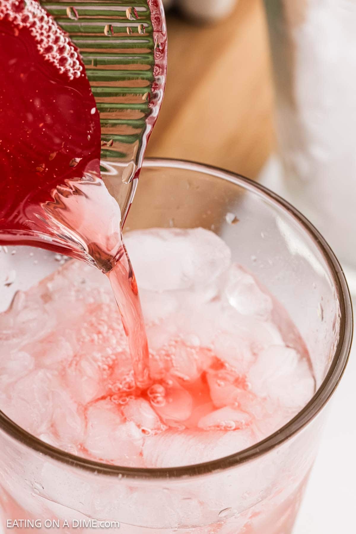 Strawberry syrup being poured into a glass with ice and Sprite.