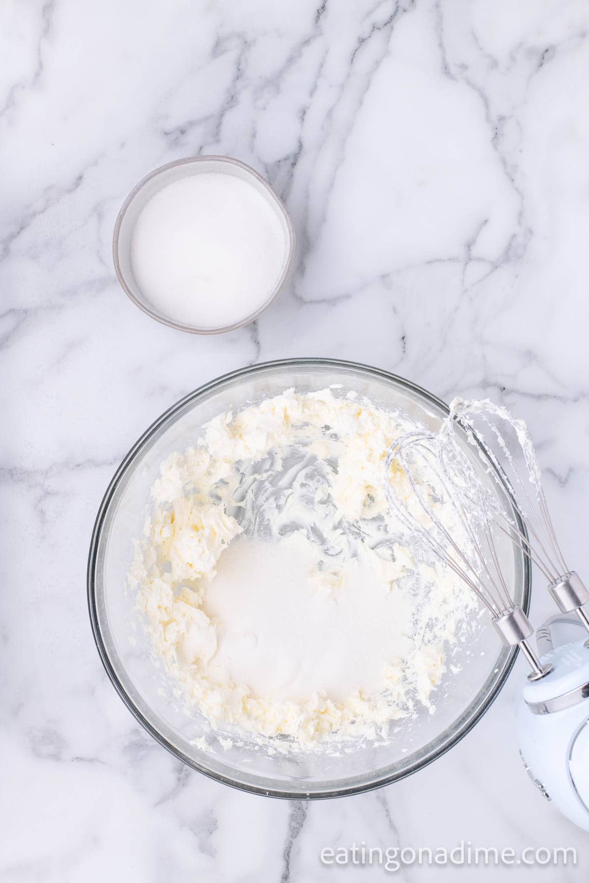 Cream cheese and sugar mixed together in a bowl with a small bowl of heavy cream on the side