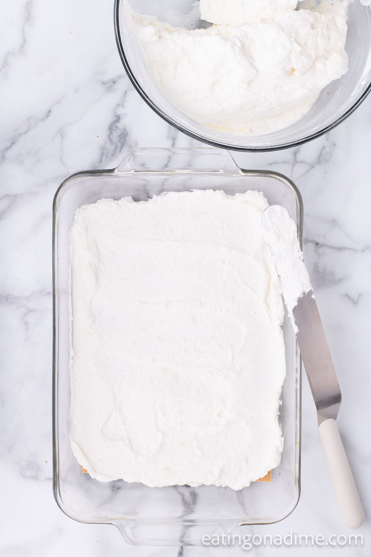 Spreading the cream layer on the graham crackers in the baking dish with a bowl of cream cheese mixture