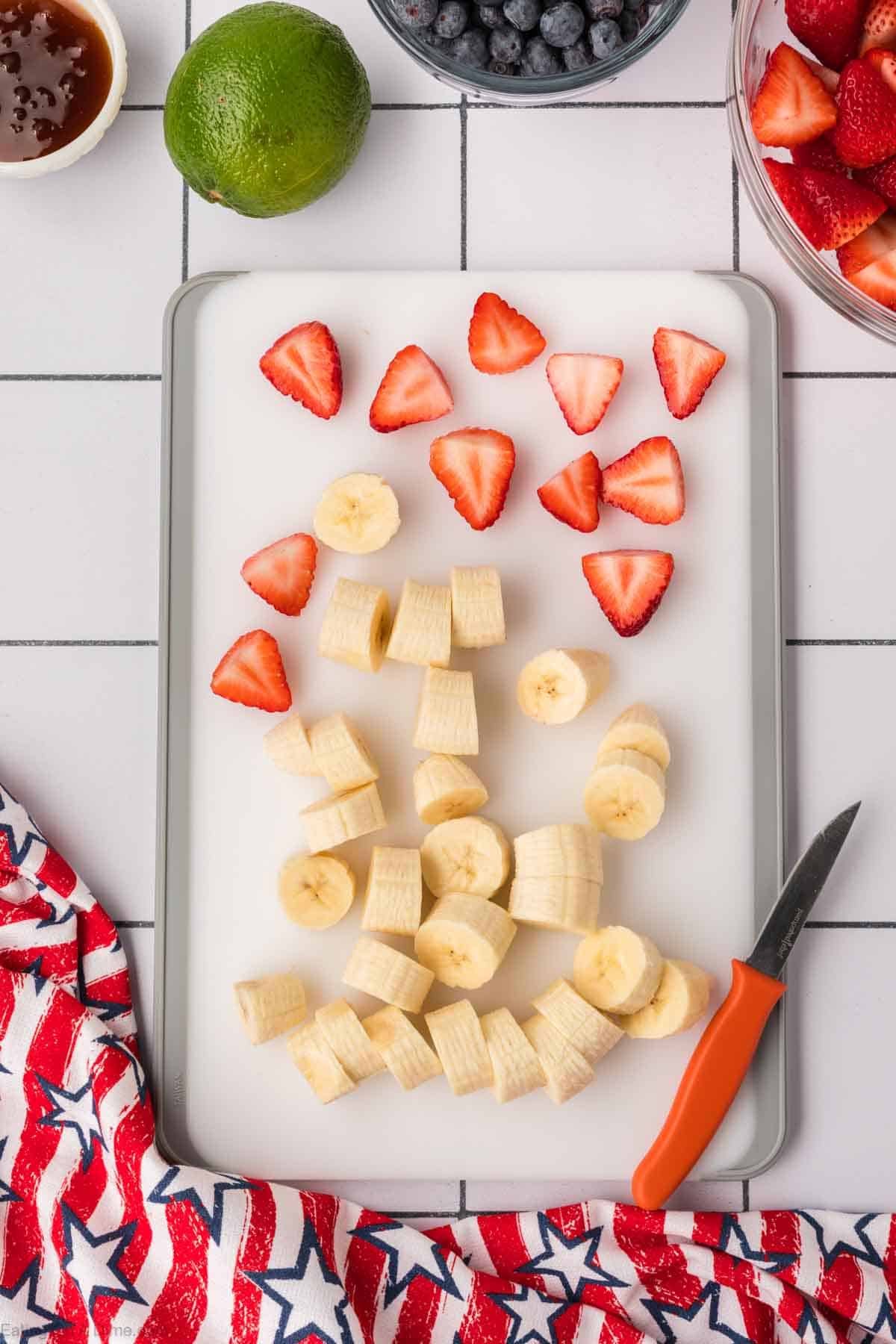 Sliced bananas and strawberries on a cutting board with a knife