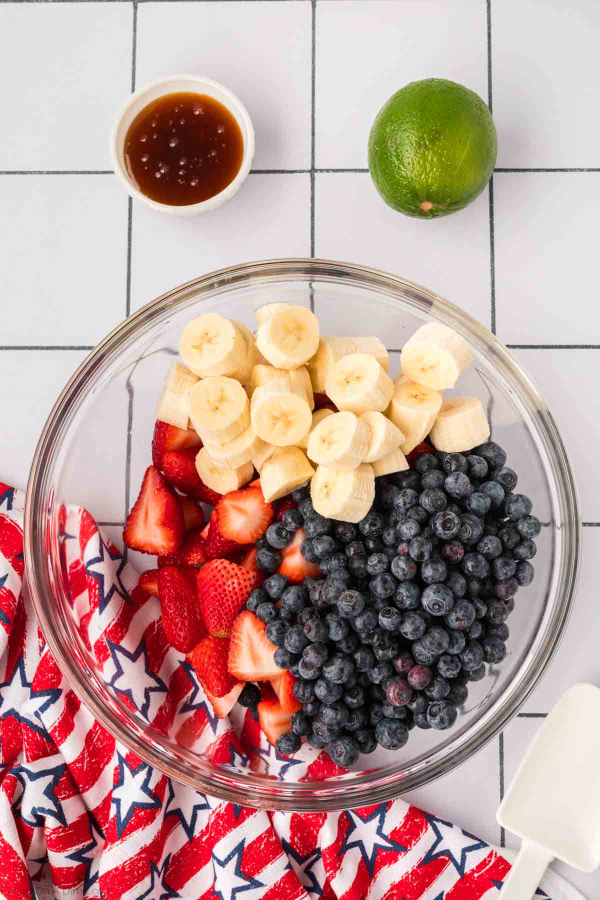 Blueberries, strawberries and bananas in a bowl with a small bowl of honey and fresh lime on the side