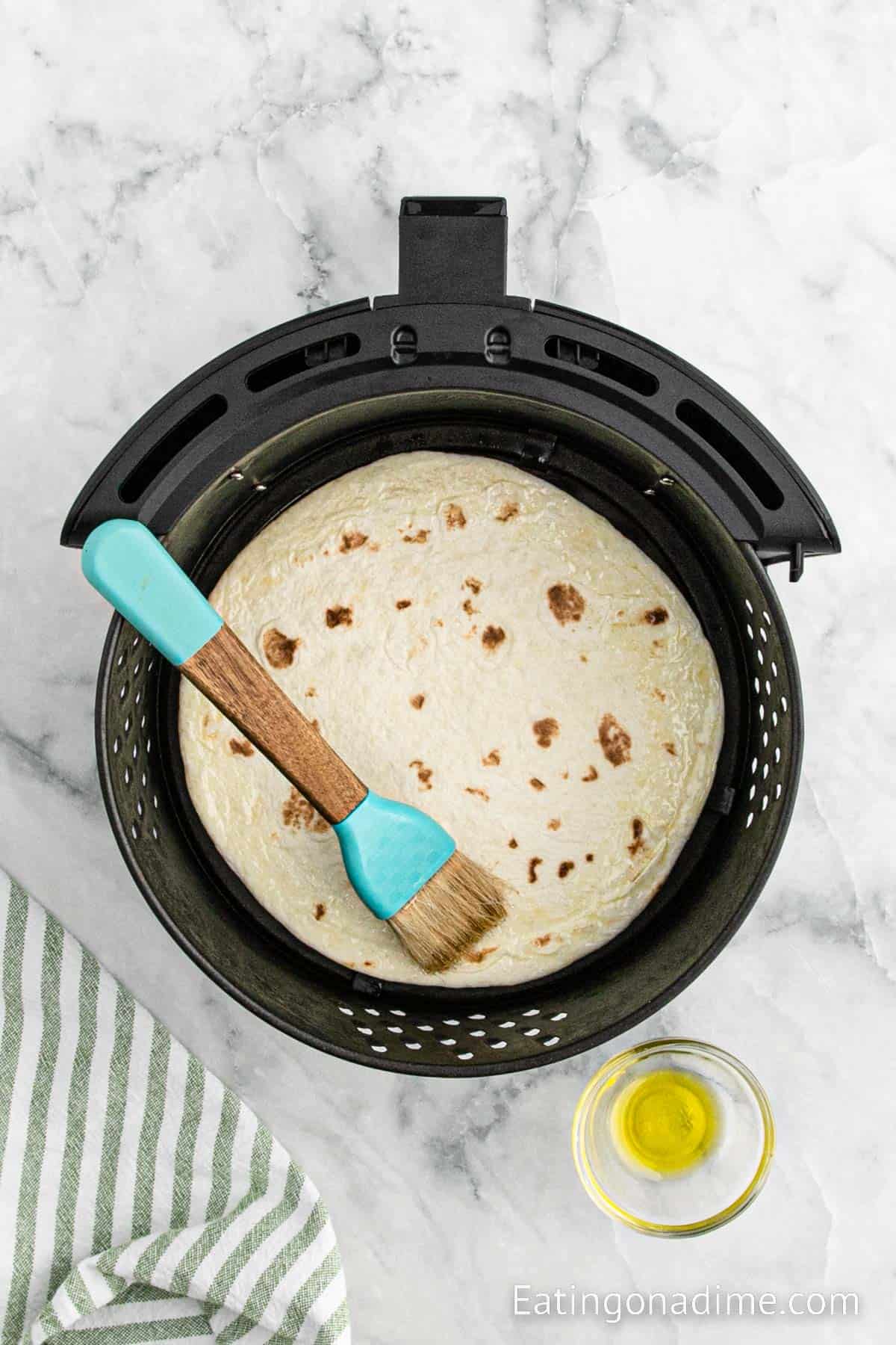 Placing tortilla in the air fryer basket and brush oil over the tortilla