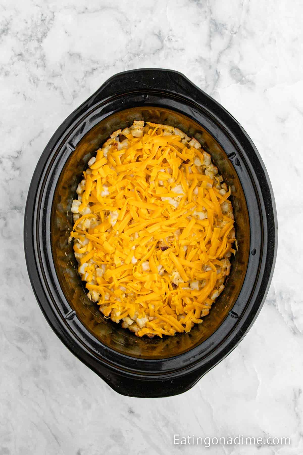 Top the hashbrown mixture with shredded cheese in the slow cooker
