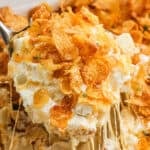 Funeral Potatoes in a baking dish with a serving on a spoon.