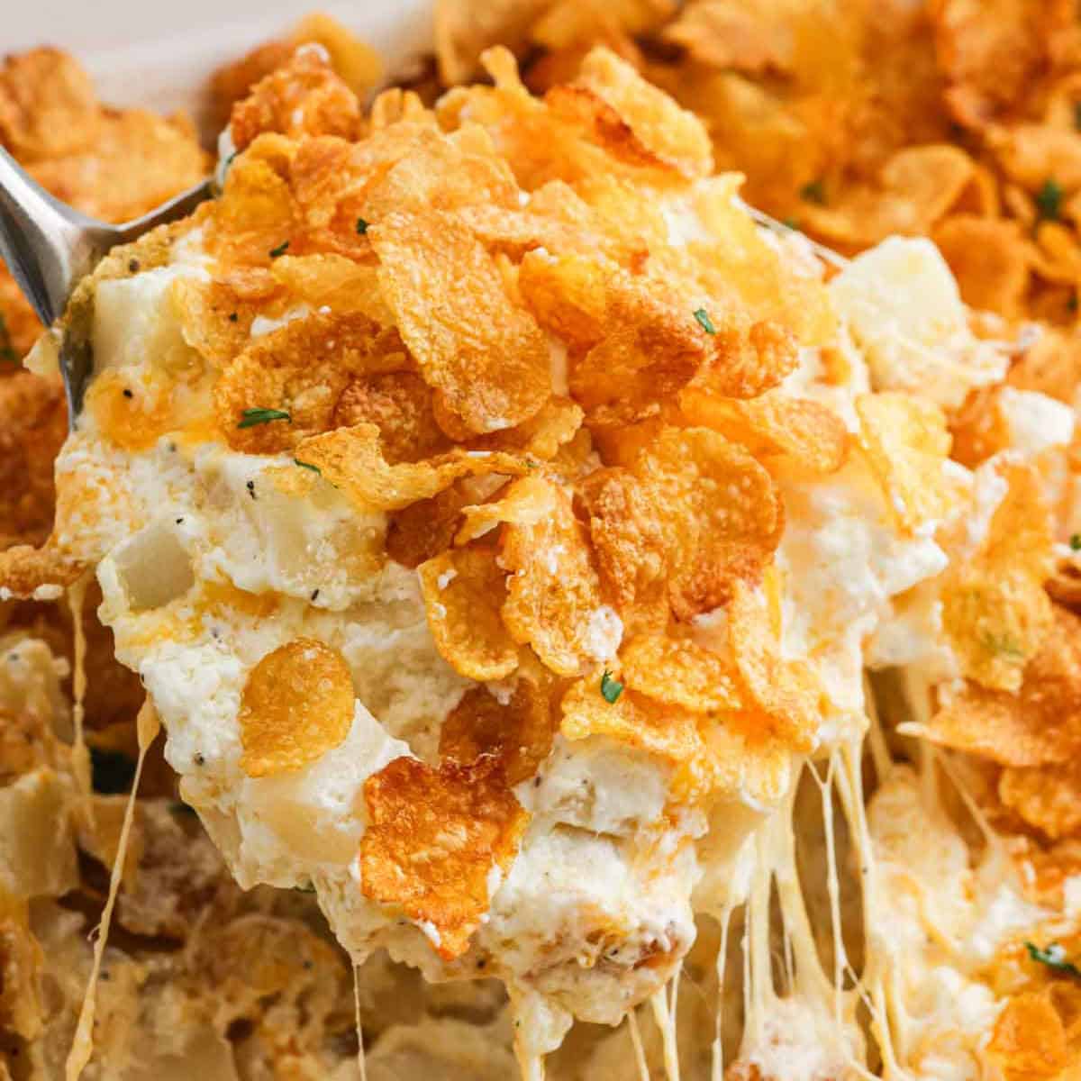 Funeral Potatoes in a baking dish with a serving on a spoon.