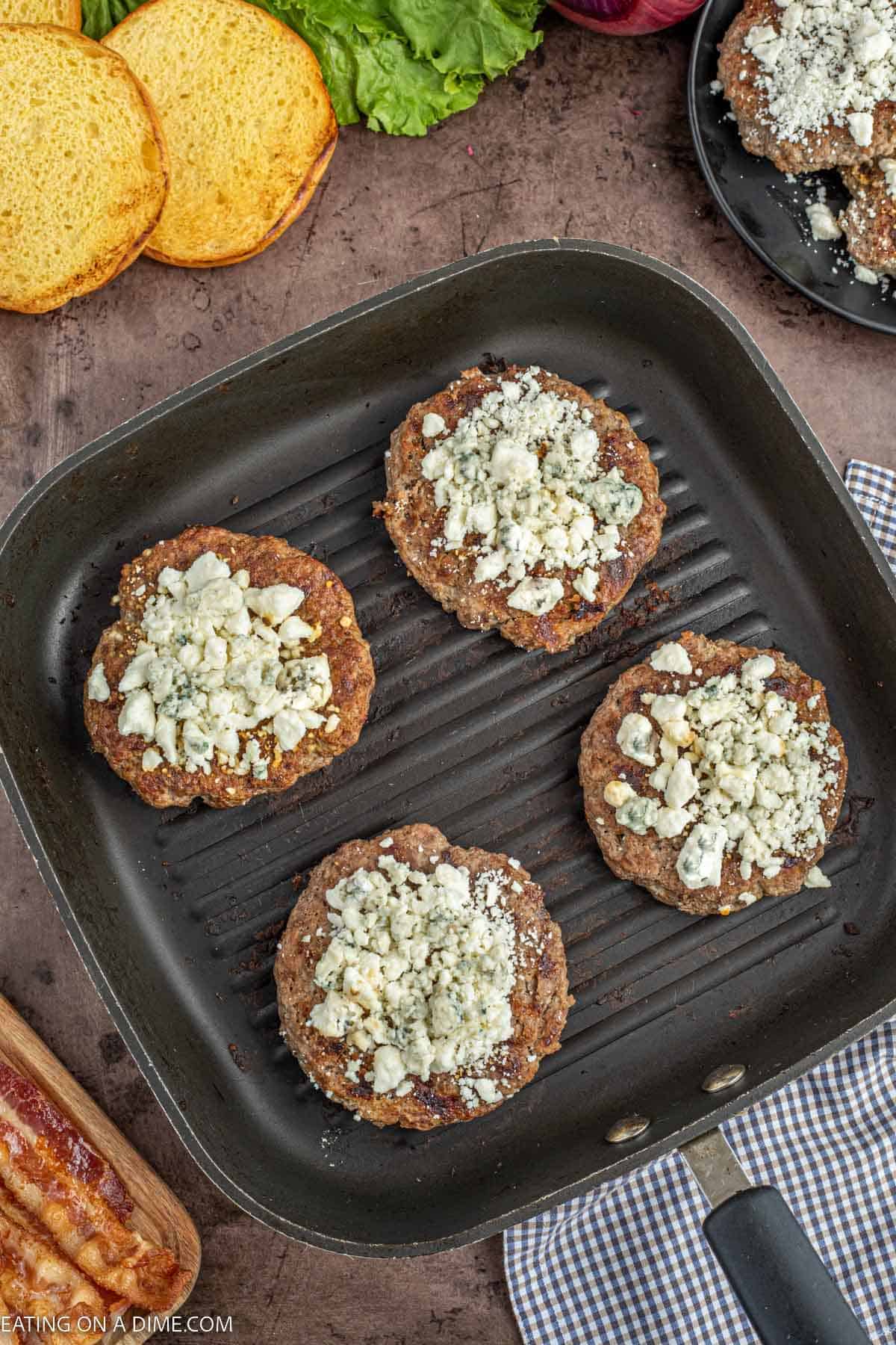 Cooking hamburger patties on skillet topped with blue cheese crumbles