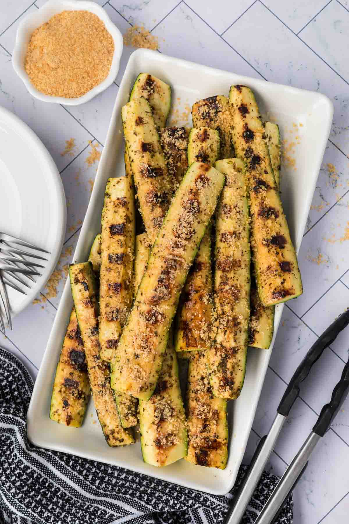 Parmesan Grilled Zucchini spears stacked on a white platter. 