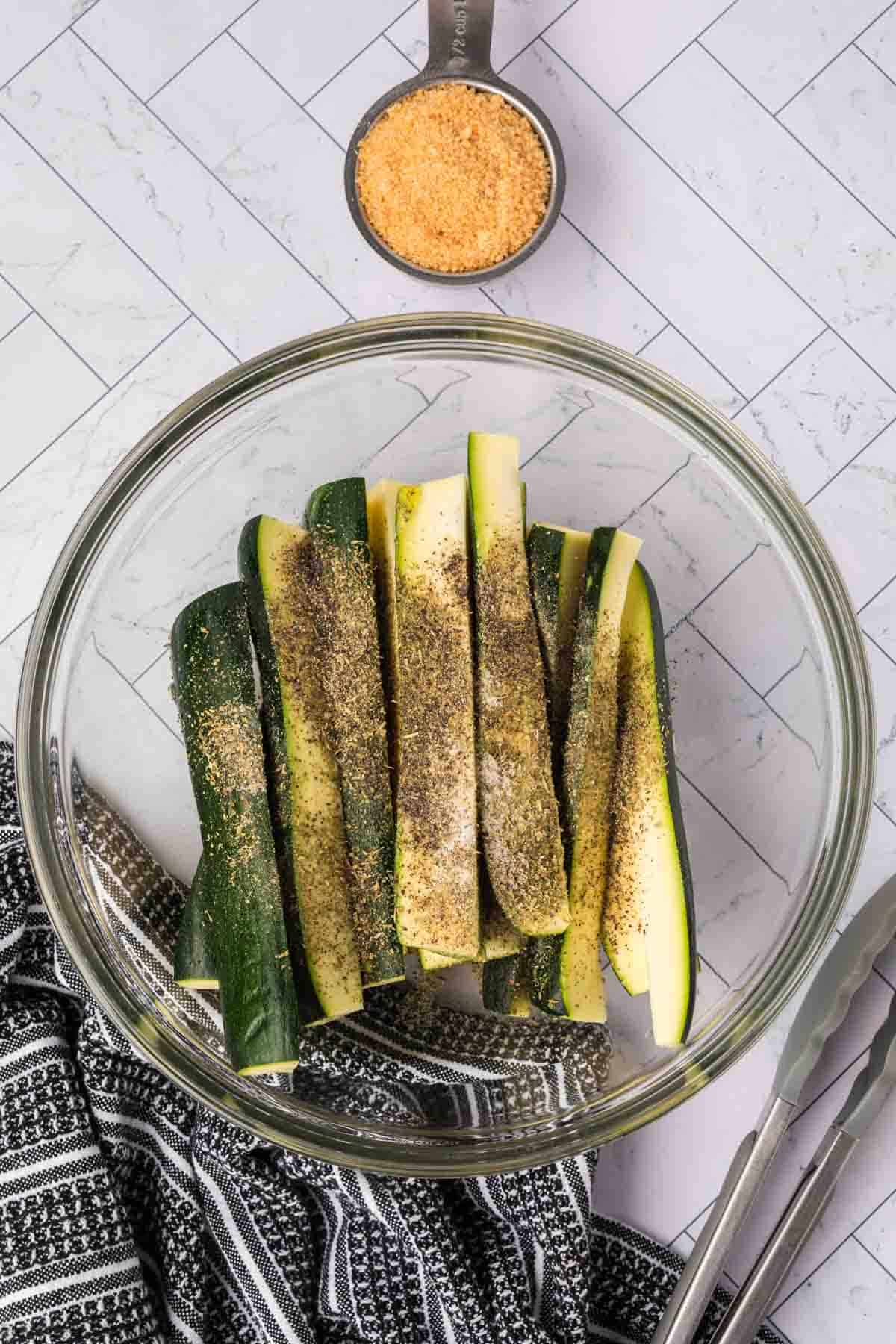 Zucchini spears in a bowl topped with seasoning