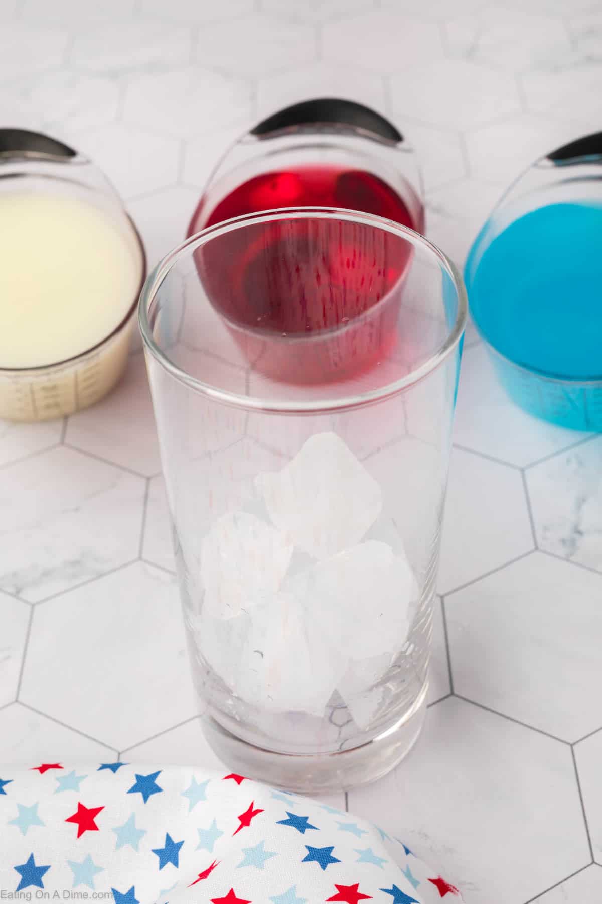 Ice cubes in a glass with small containers with pina colada, cranapple juice, and blue gatorade