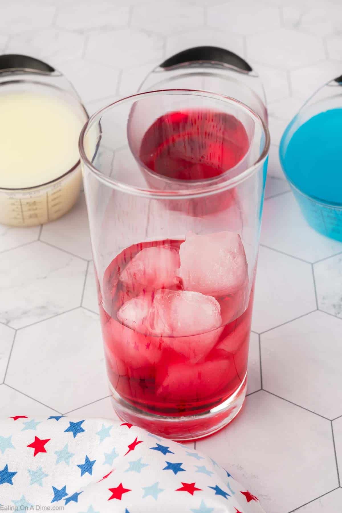 Red juice in a glass with ice with small containers of pina colada, red juice and blue gatorade 